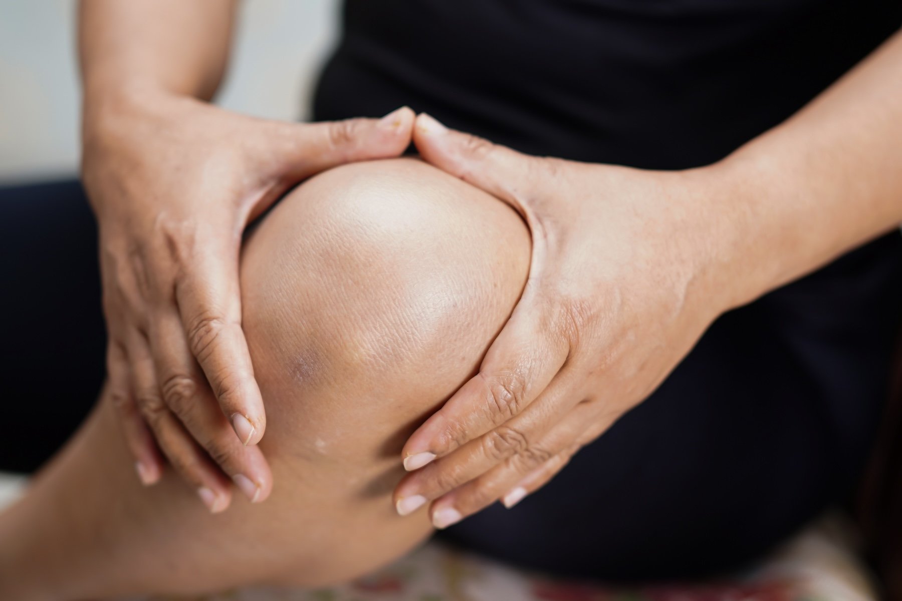 Close-up of a person receiving a knee massage or physical therapy on their right knee, with hands gently holding and supporting the knee.