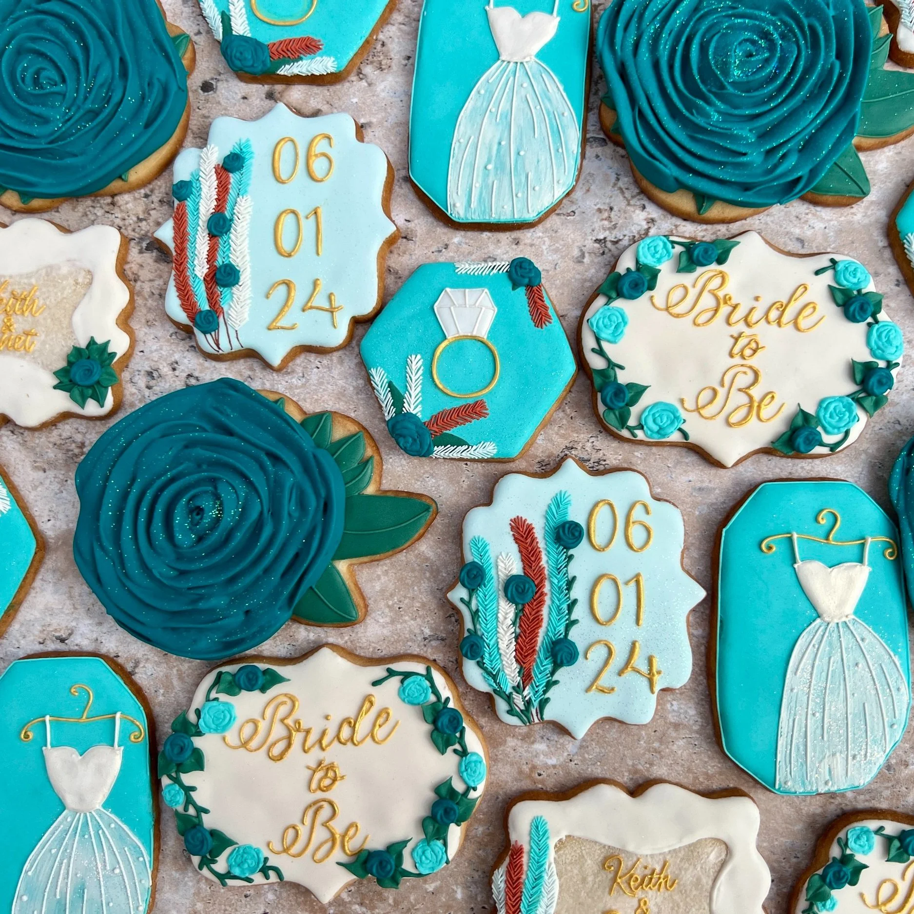 An assortment of wedding-themed cookies in various shapes and colors, decorated with icing. The cookies feature phrases like "Bride to Be" and decorative elements such as roses, feathers, and a wedding dress with an engagement ring.