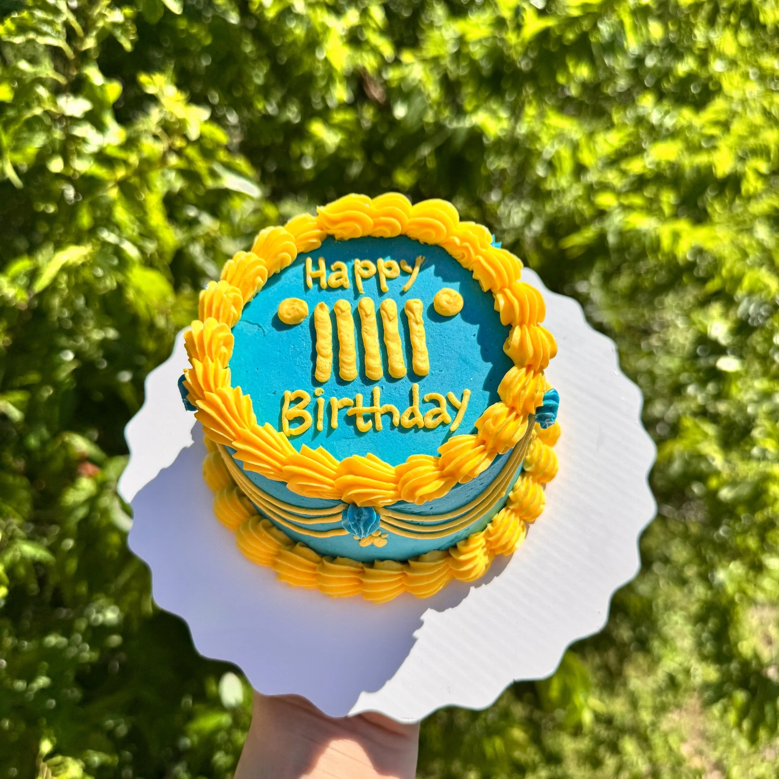 Blue birthday cake with yellow piping and decoration, with a message that reads "Happy IIIII Birthday"