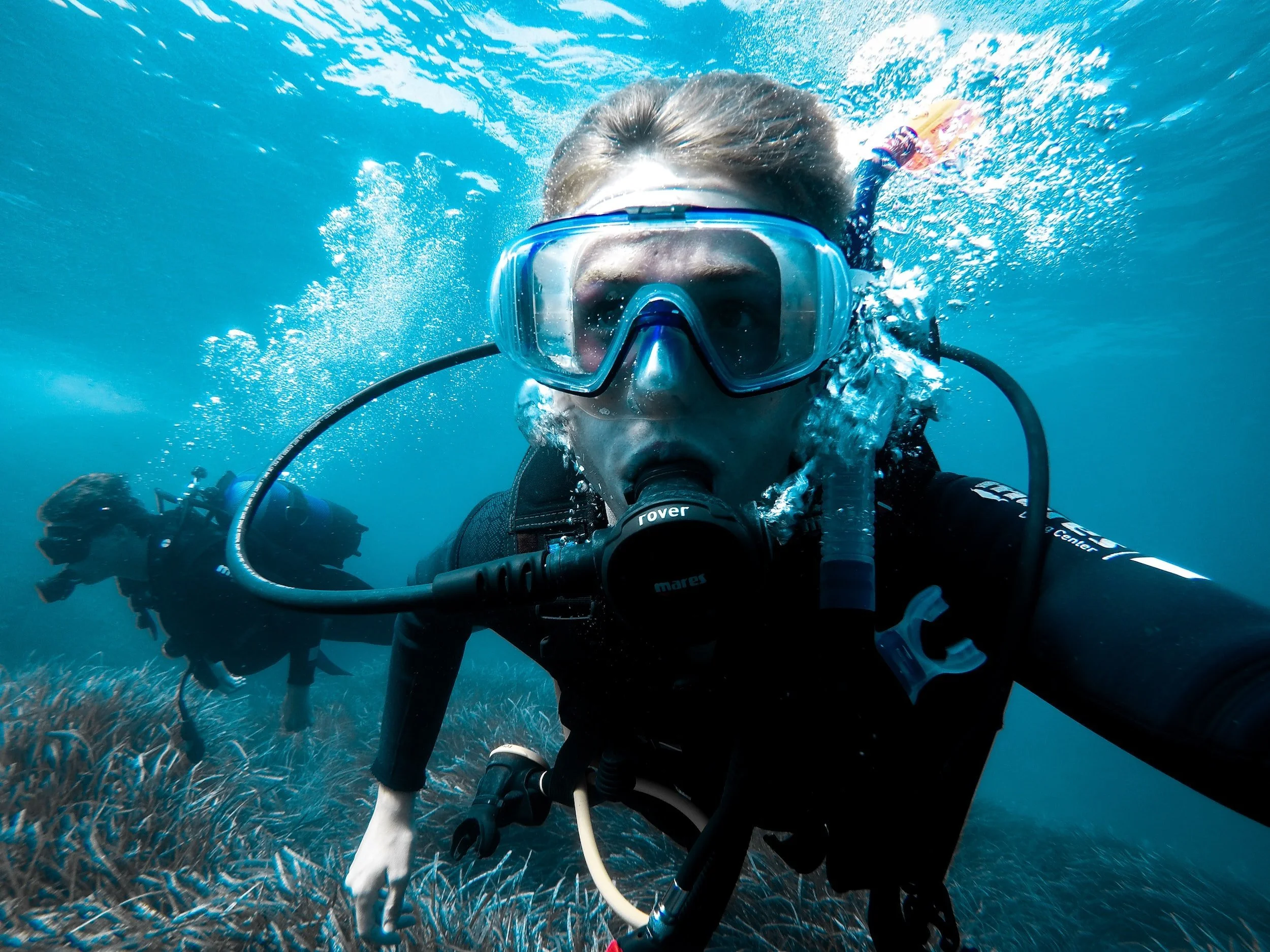 Two scuba divers swimming underwater near coral reef, wearing masks and breathing through regulators.