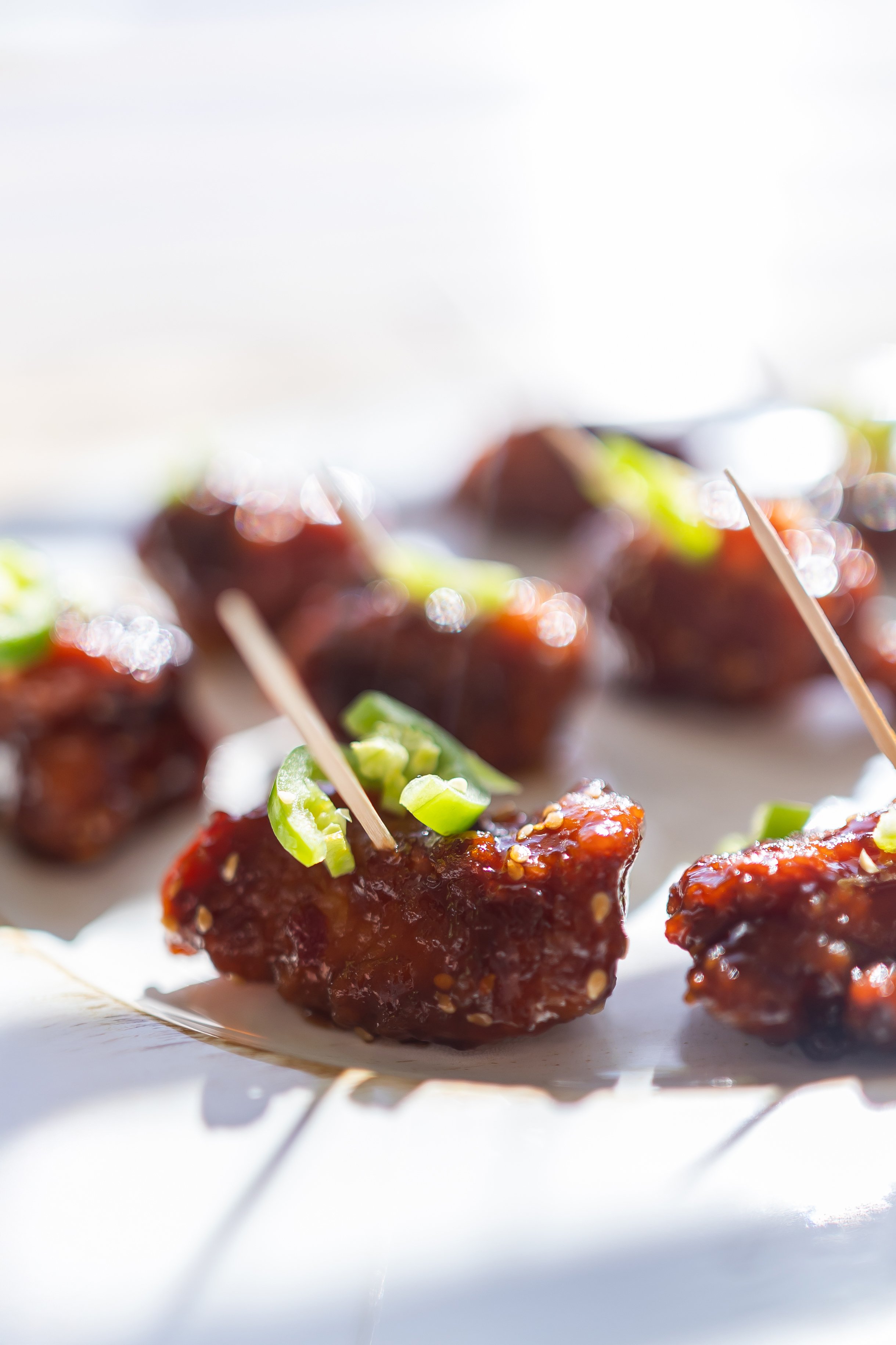 Close-up of glazed meat appetizers with toothpicks and green garnishes on a plate.