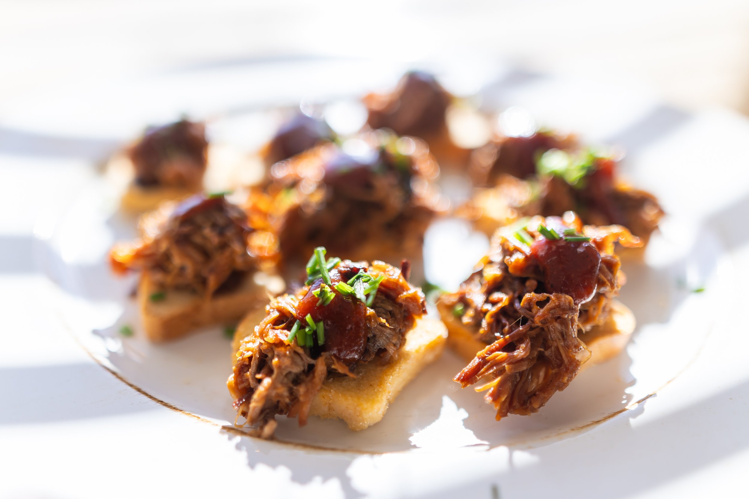 Plate of pulled pork appetizers with barbecue sauce and chives on toasted bread.