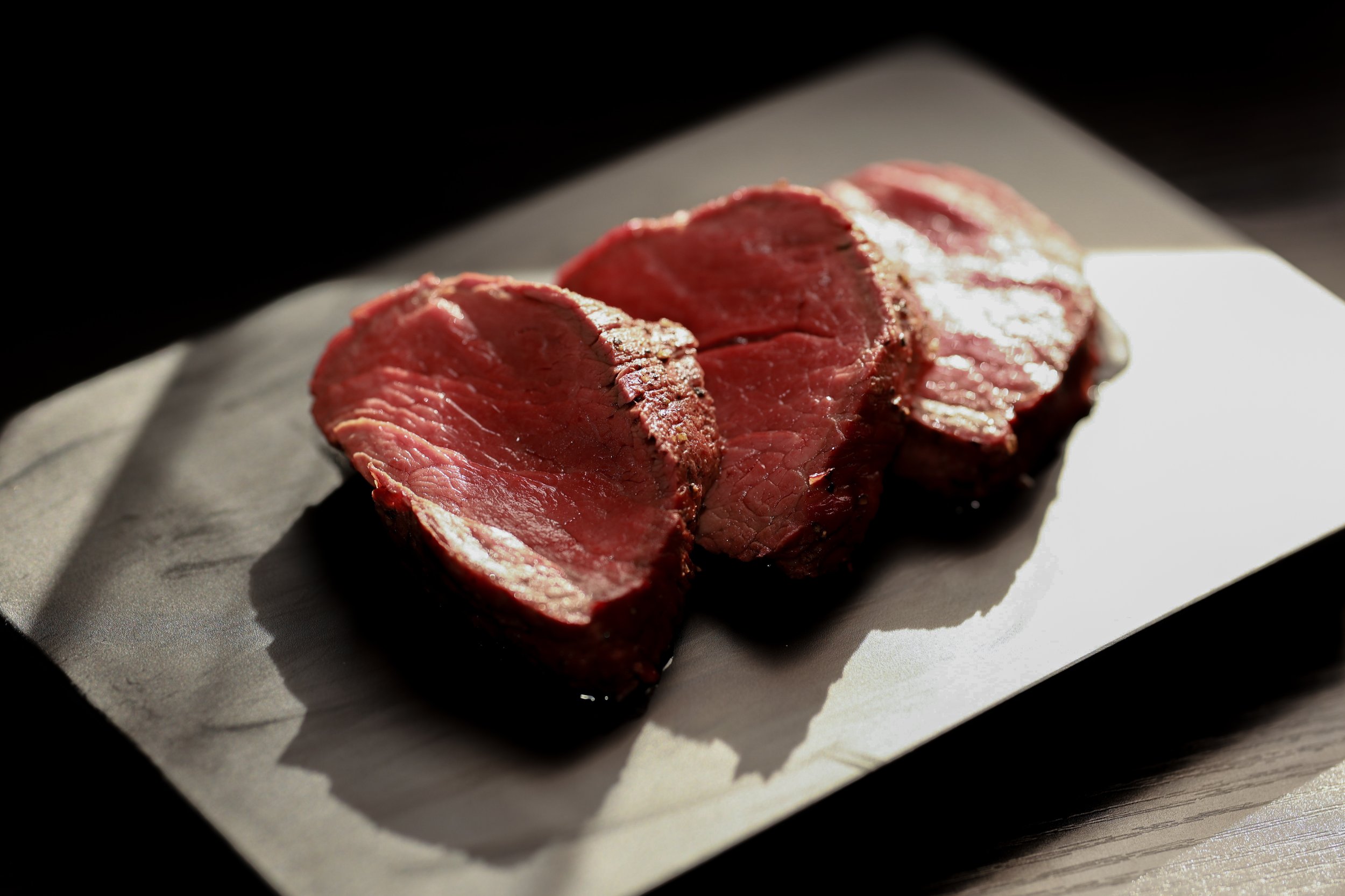 Three slices of cooked meat on a rectangular white plate