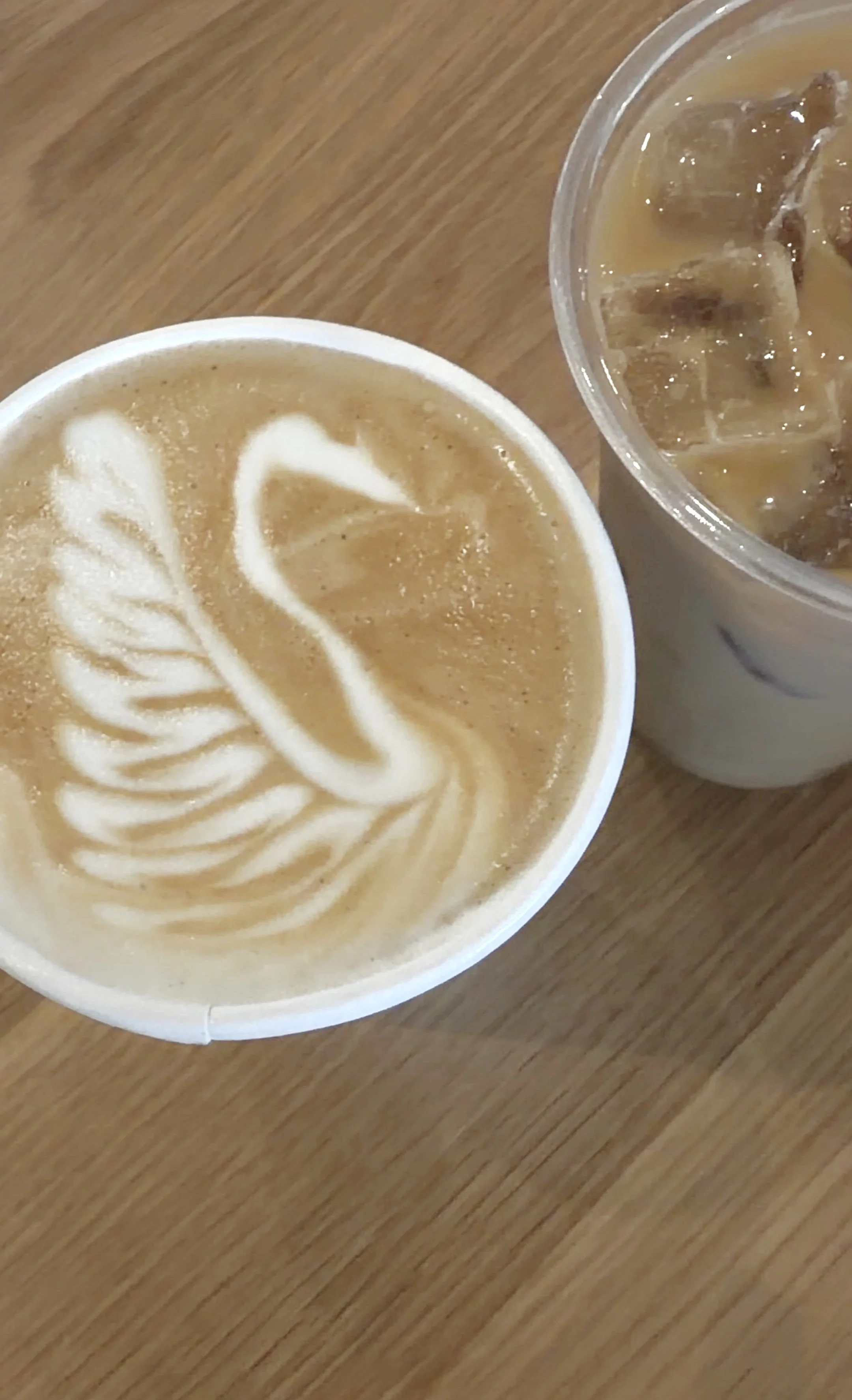 A cup of coffee with latte art and a glass of iced coffee on a wooden table.