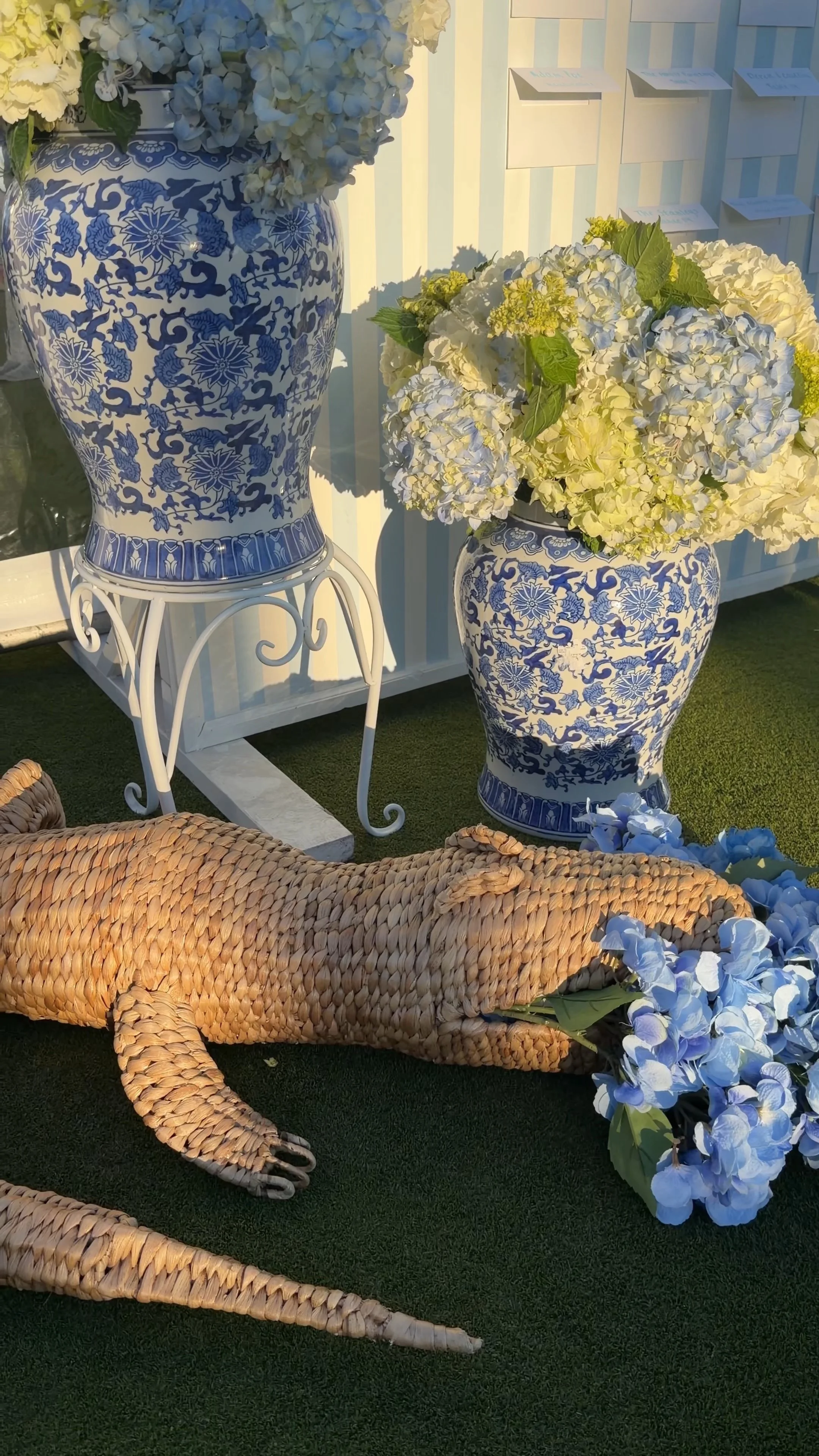 White and blue floral ceramic vases with hydrangea flowers placed on decorative white metal stands, with a woven wicker crocodile sculpture in the foreground at a luxury wedding, by wilmington content co - content creator in north carolina