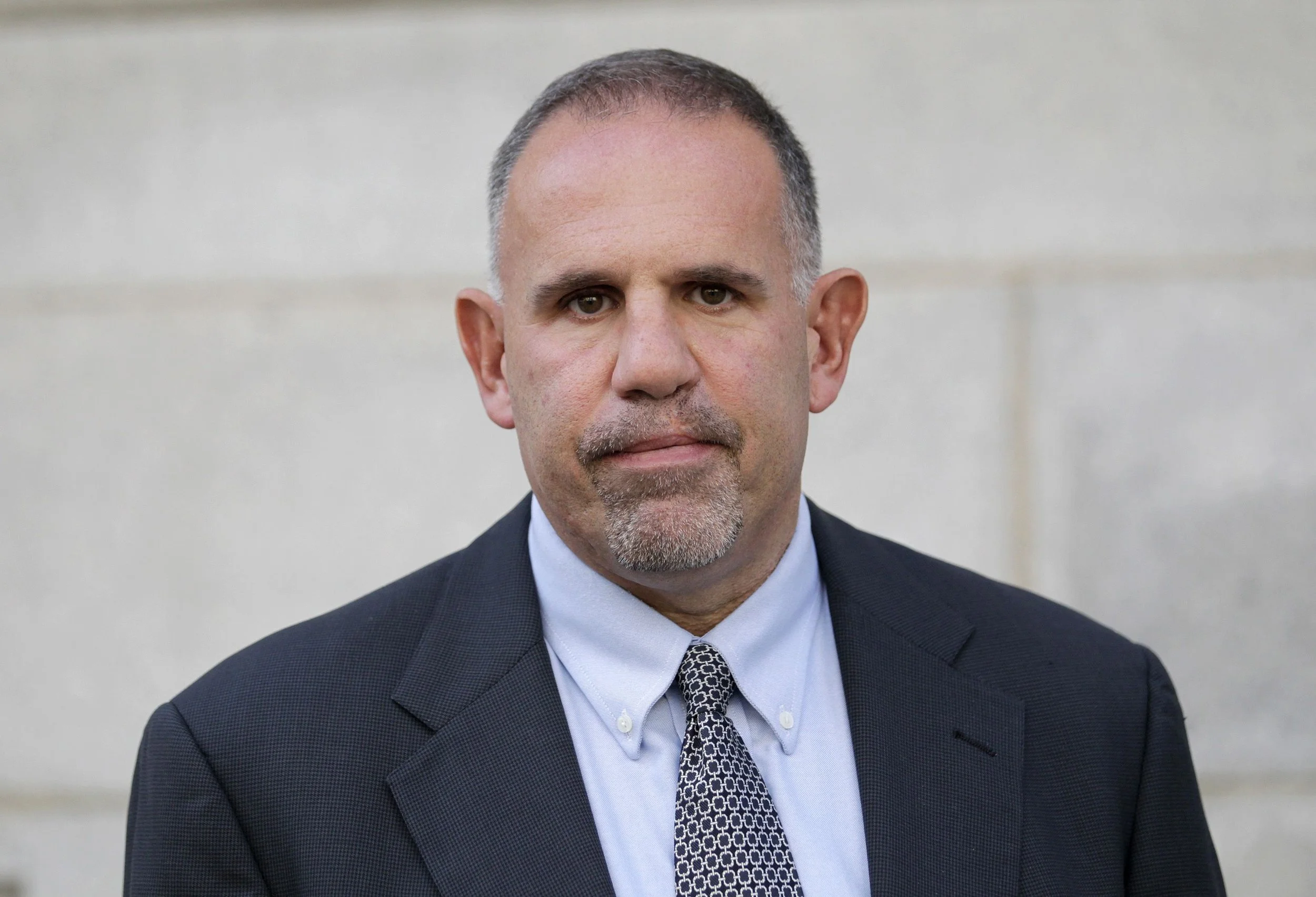 A middle-aged man in a suit and tie, with short hair and a goatee, standing against a plain background.
