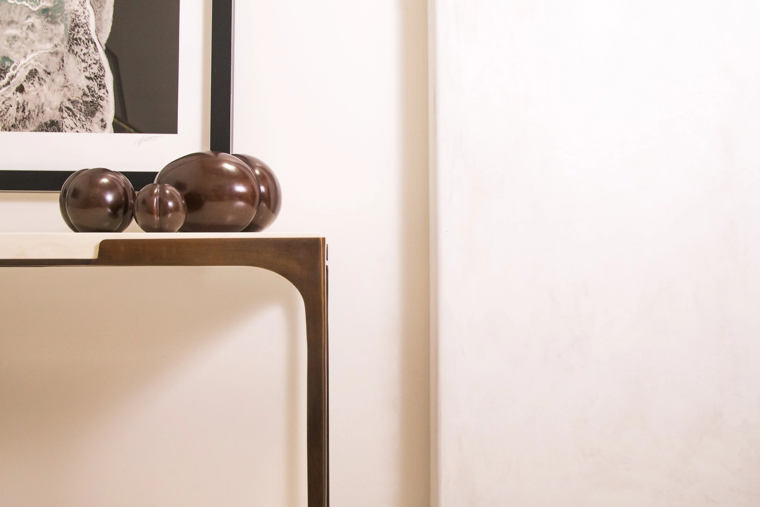 Decorative wooden sculpture resembling a set of rounded stones on a wooden table, with a framed black and white photograph partially visible in the background.