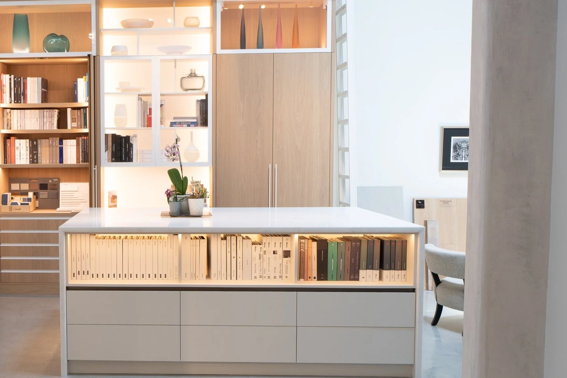 Modern interior with bookshelves, decorative vases, and a white kitchen island with a plant on top.