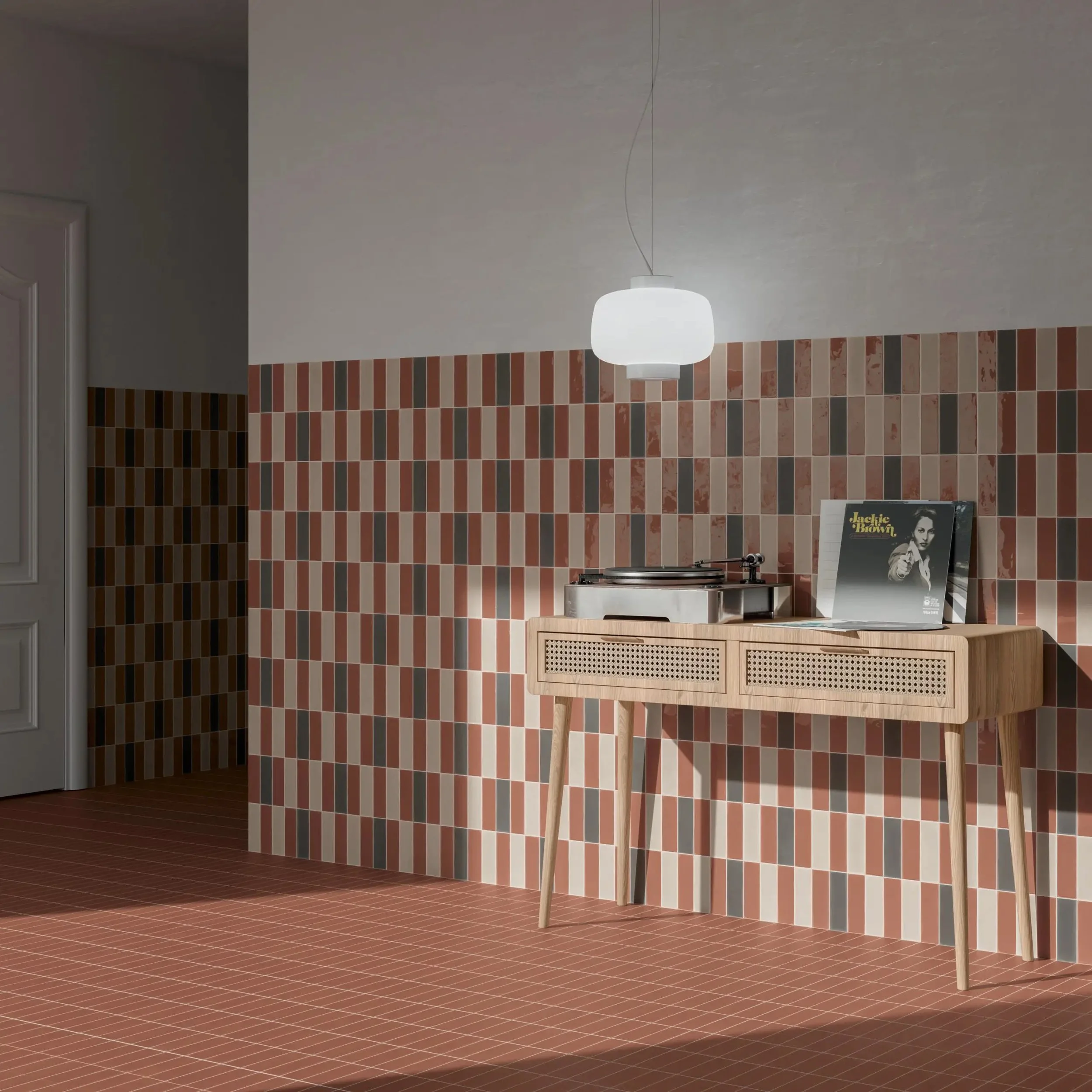 A room with patterned tile walls and floor, a wooden sideboard with a record player on top, and vinyl records leaning against the wall, illuminated by a hanging white pendant lamp.