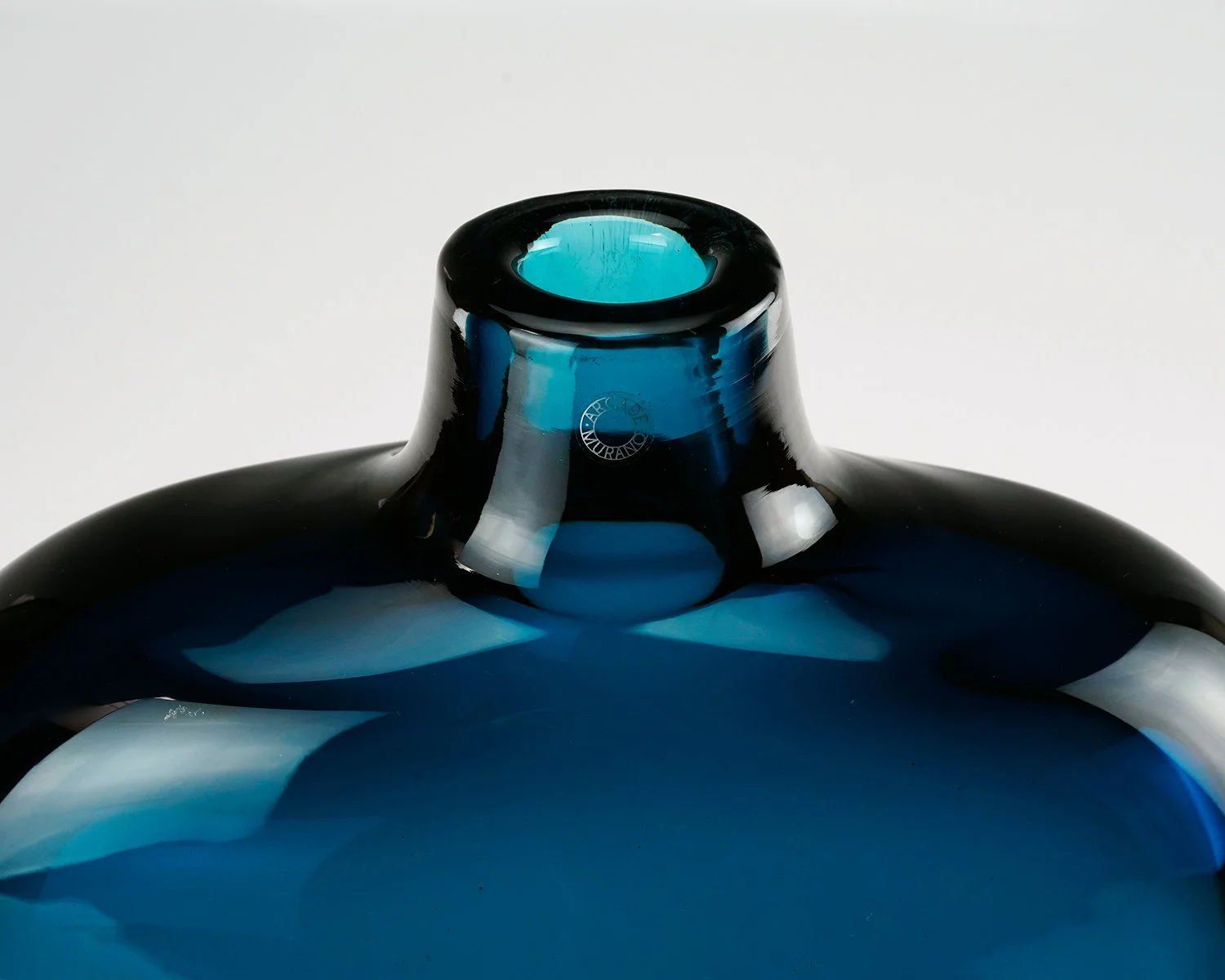 Close-up of the neck of a blue glass vase against a white background.