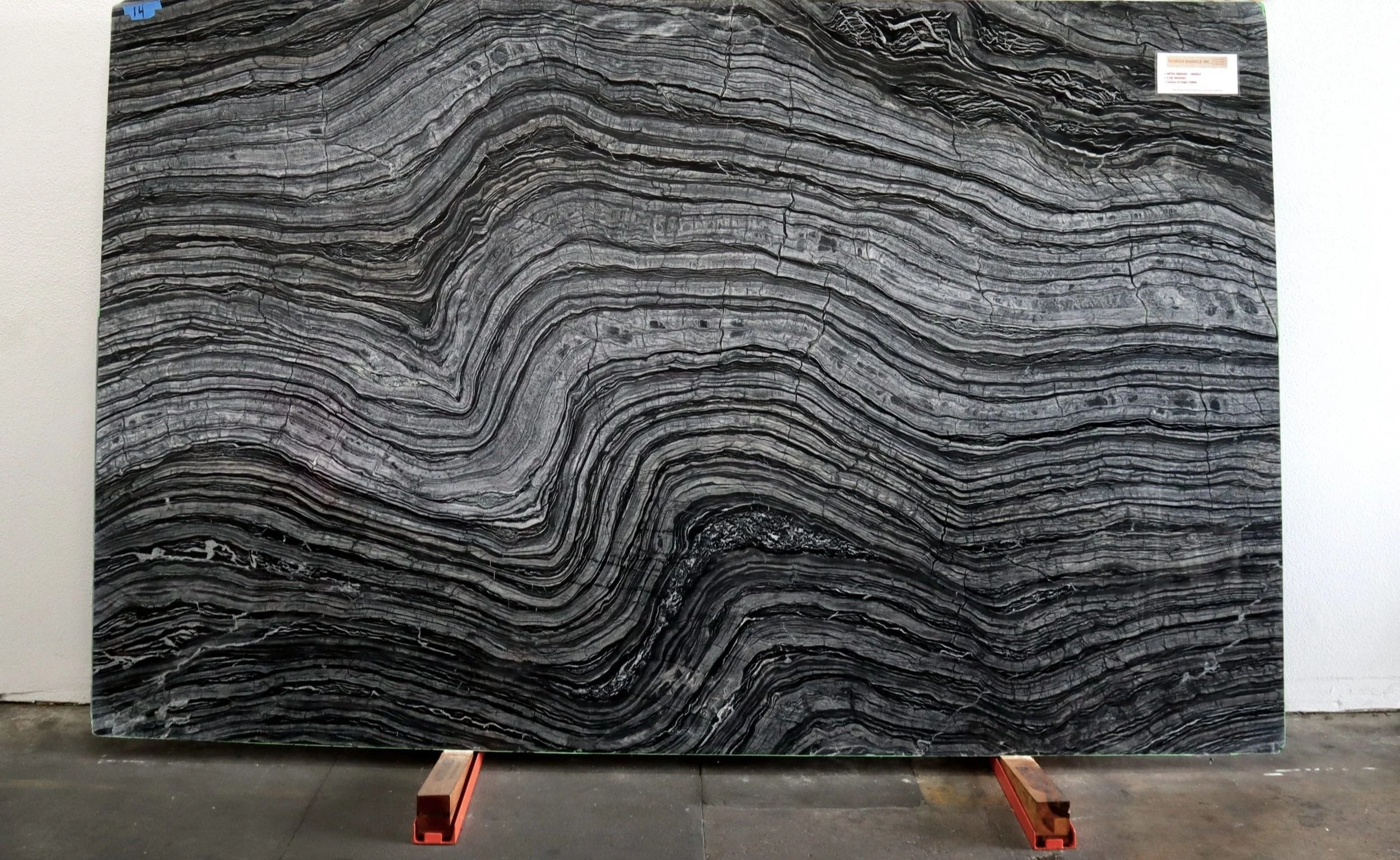 Large black and gray natural stone slab with wavy, striated patterns, set on a wooden stand indoors.