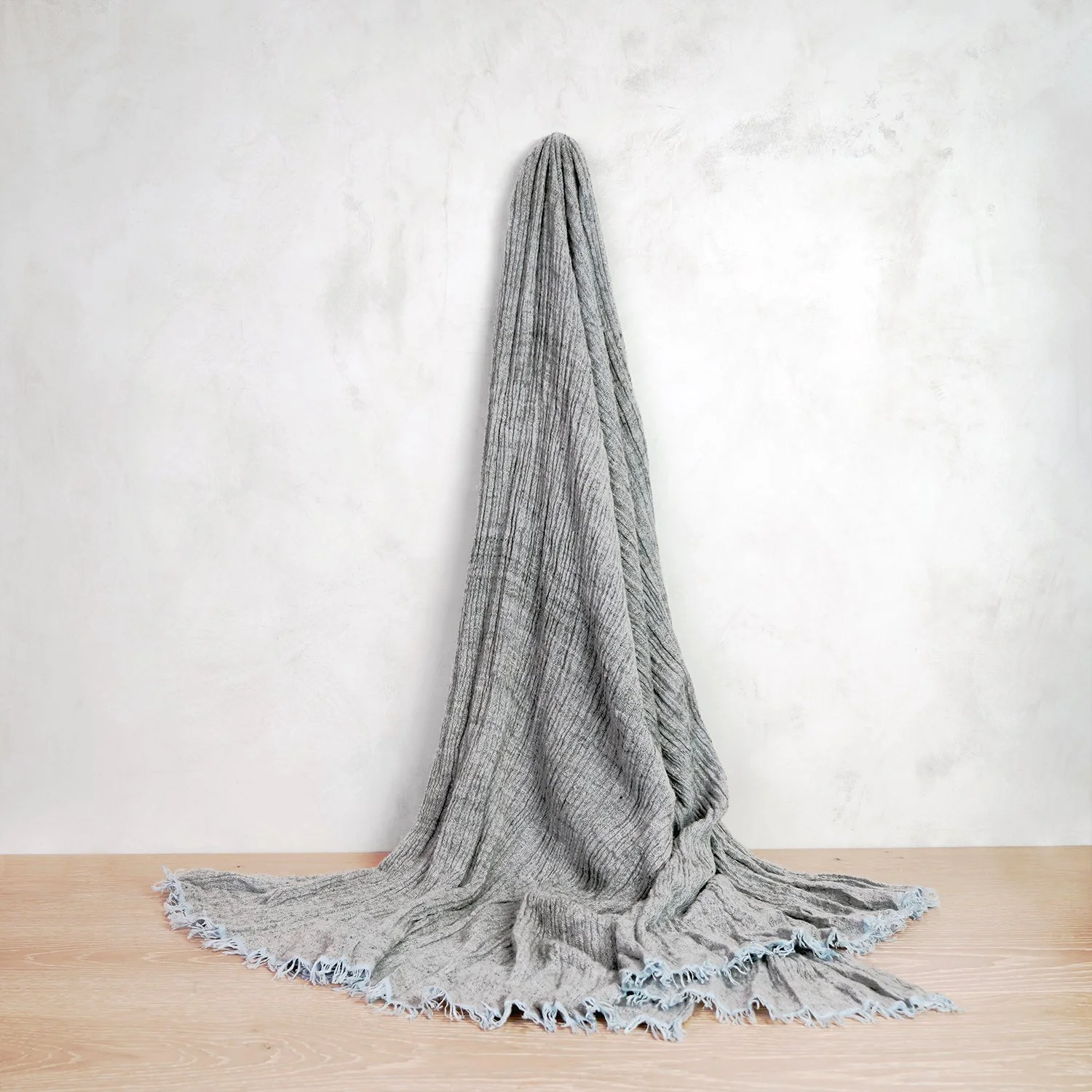 A gray blanket draped over a hook on a white wall, with the blanket pooling on a light wooden floor.