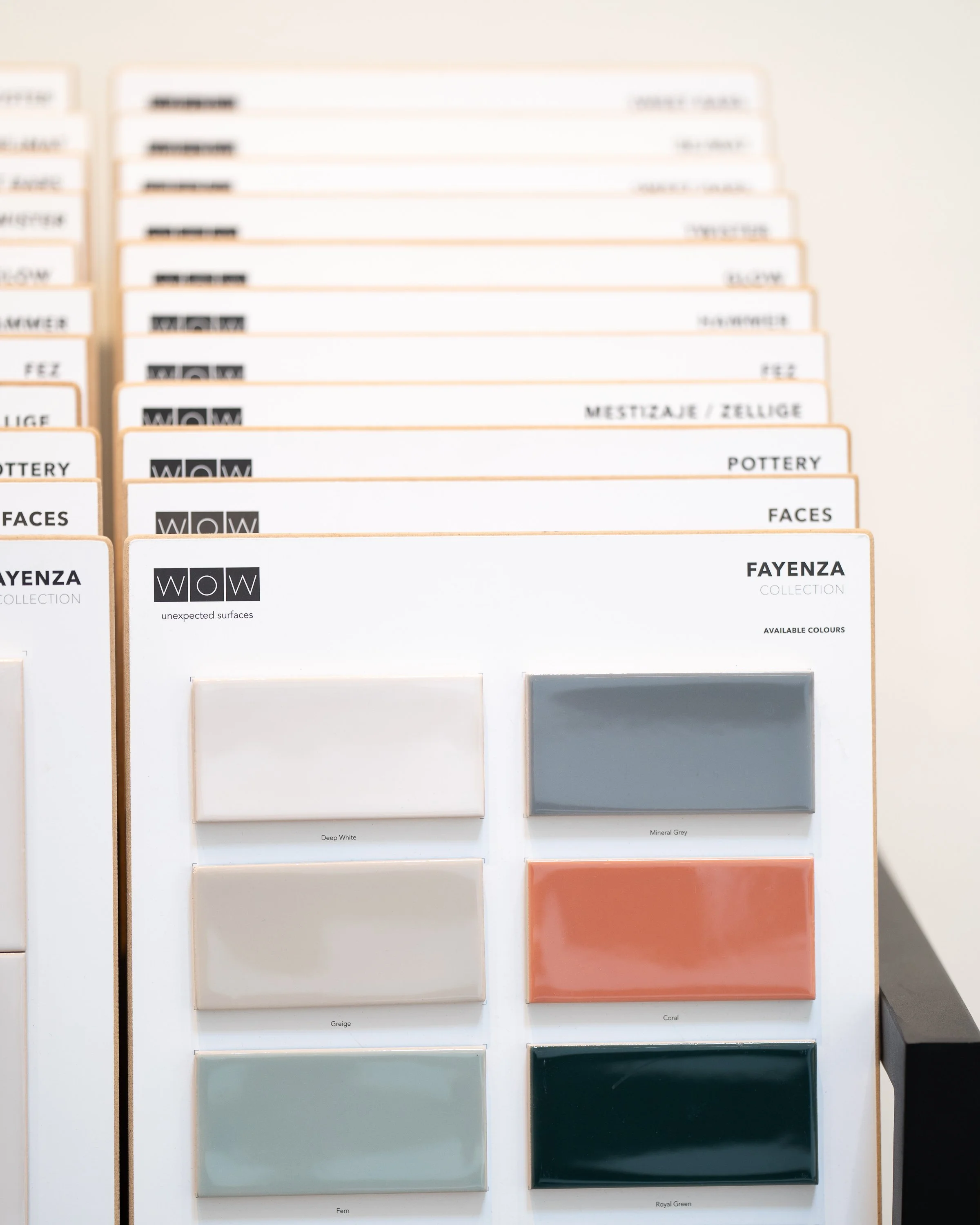 Display of ceramic color samples in a showroom, featuring shades of white, grey, beige, coral, green, and dark blue.