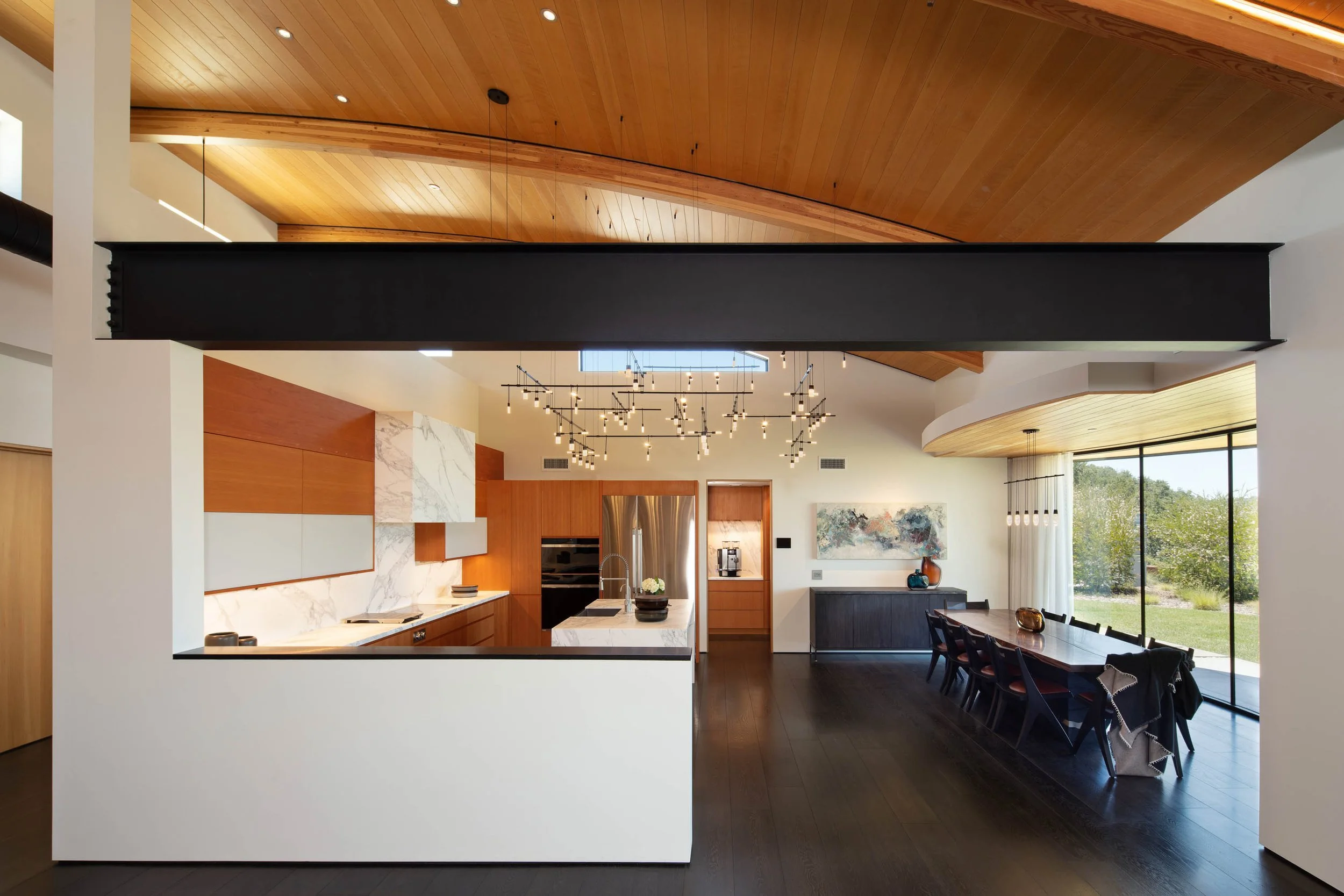 Modern open-concept kitchen and dining area with wooden ceiling, black accents, and large sliding glass doors leading outside.
