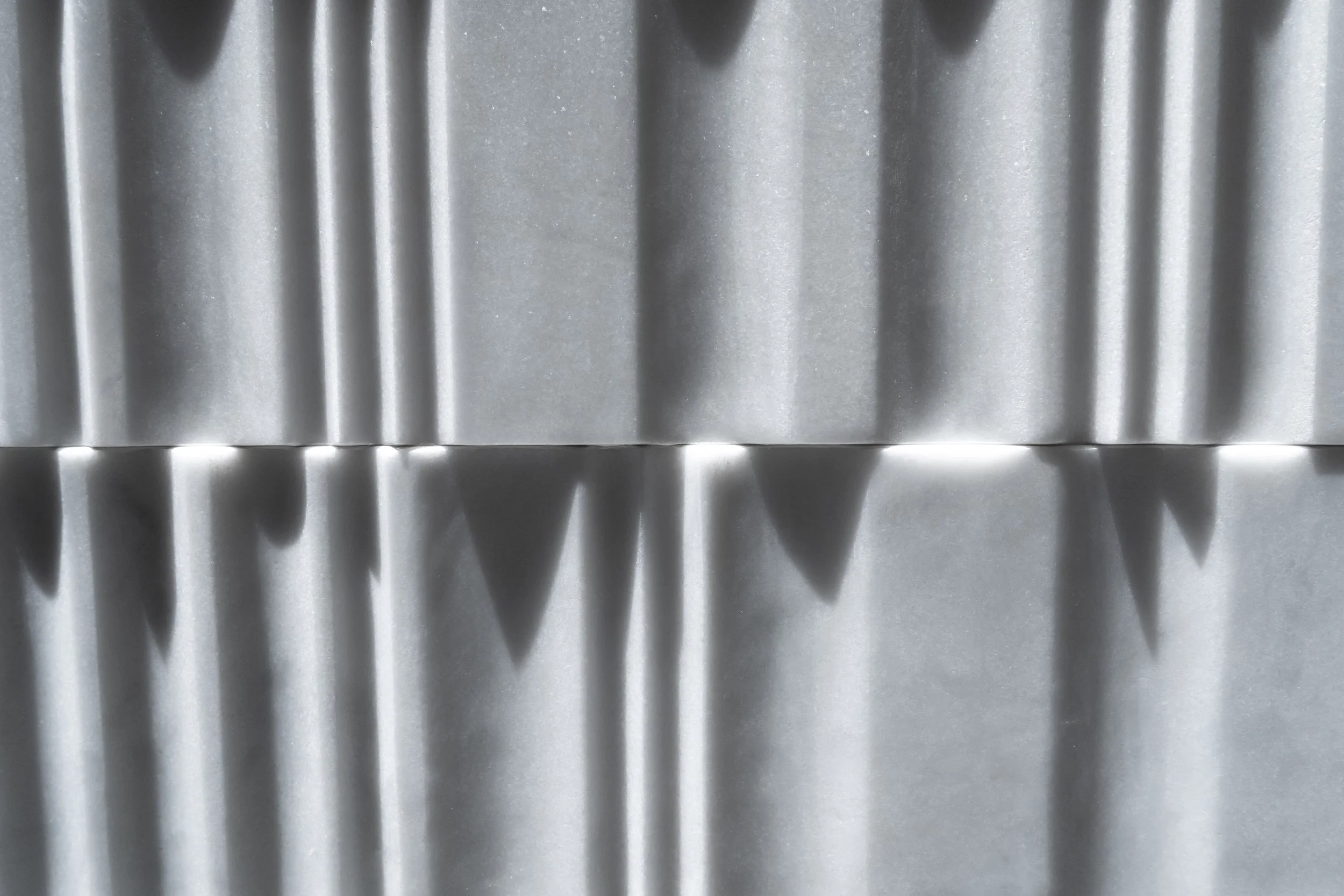 Close-up of a textured stone surface with vertical and diagonal shadows.