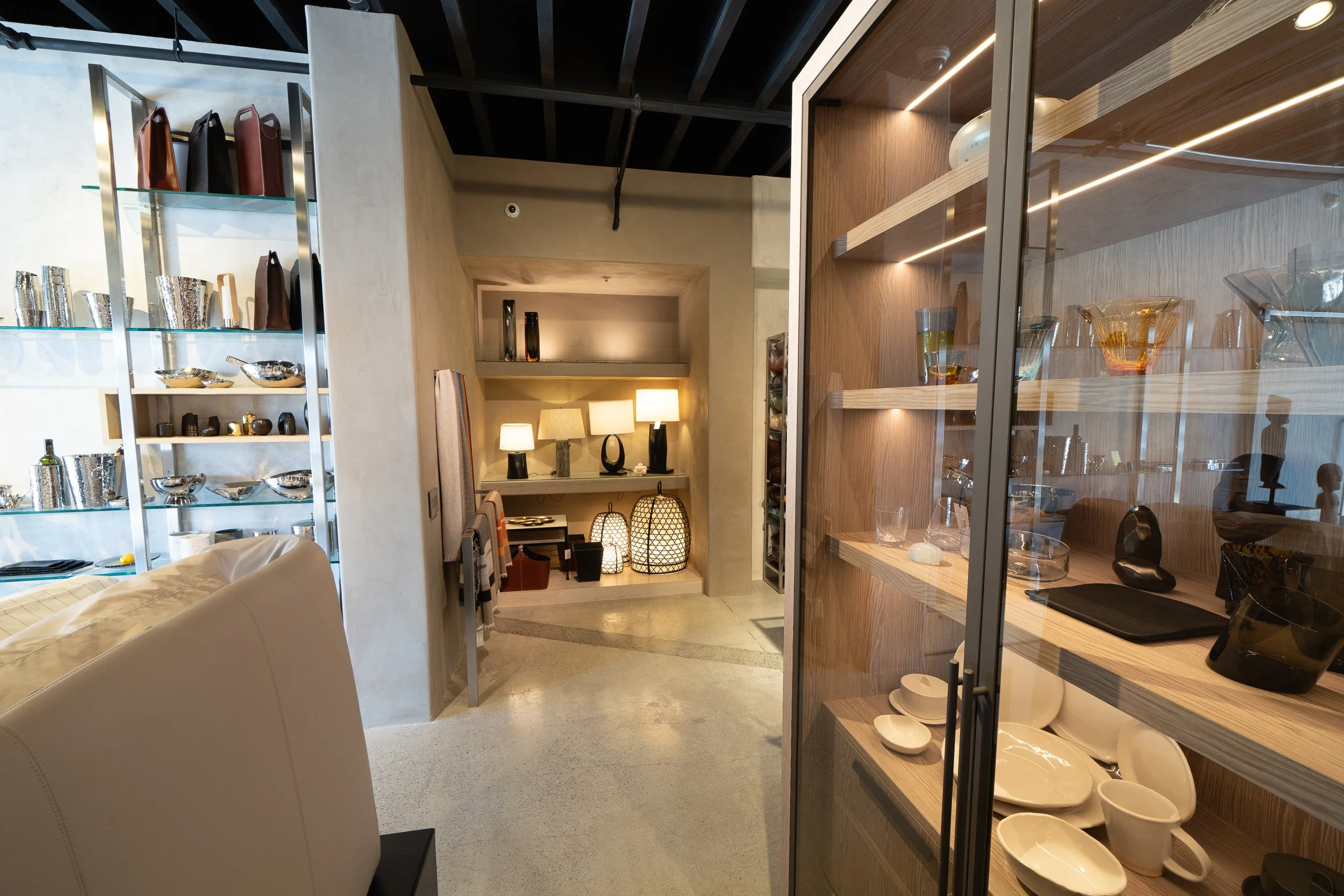 Interior view of a modern home decor store display with shelves of decorative bowls, vases, and ceramics, with lamps and lighting enhancing the scene.