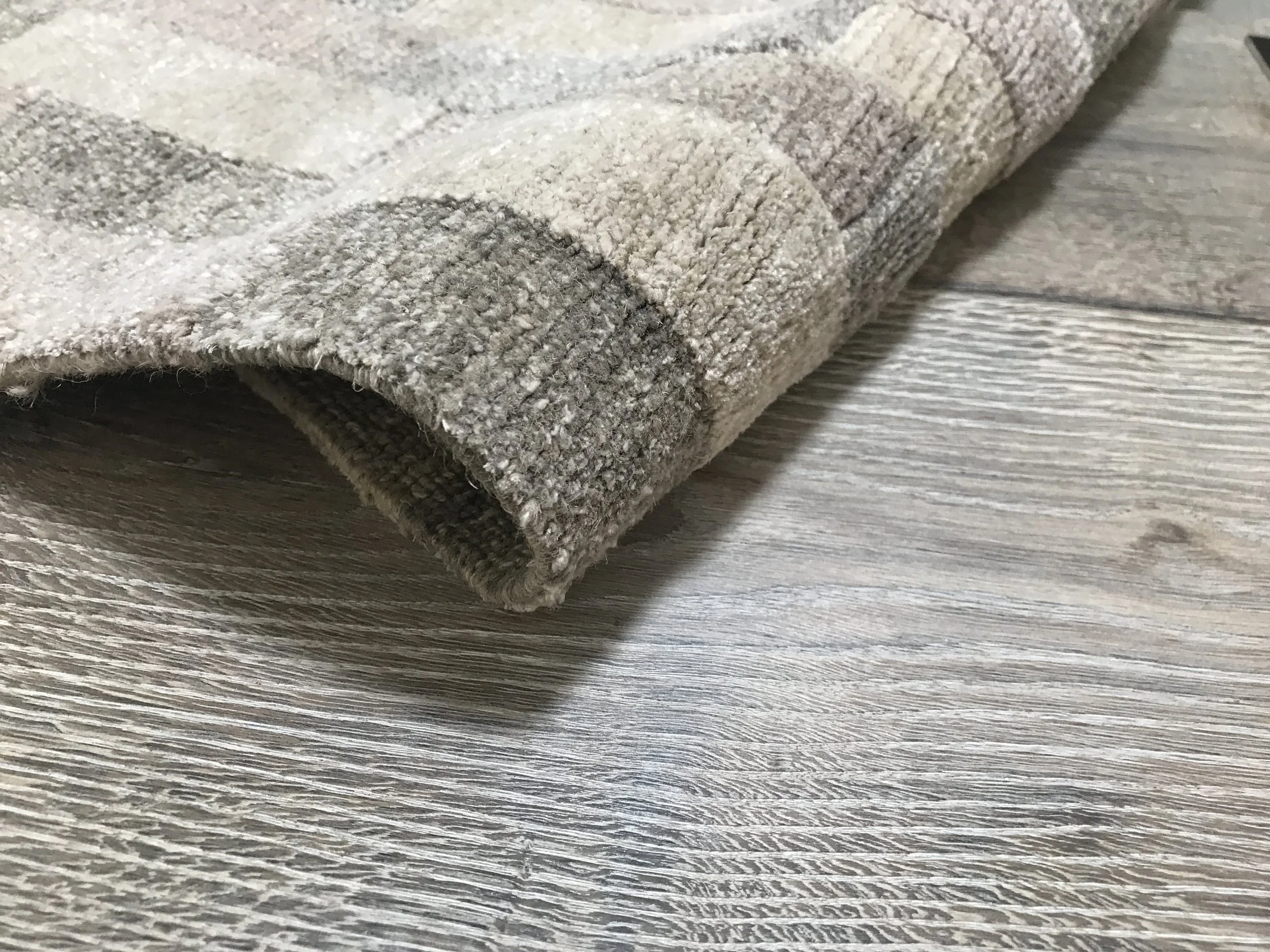 Close-up of a folded beige and gray patterned rug on a light wood floor.
