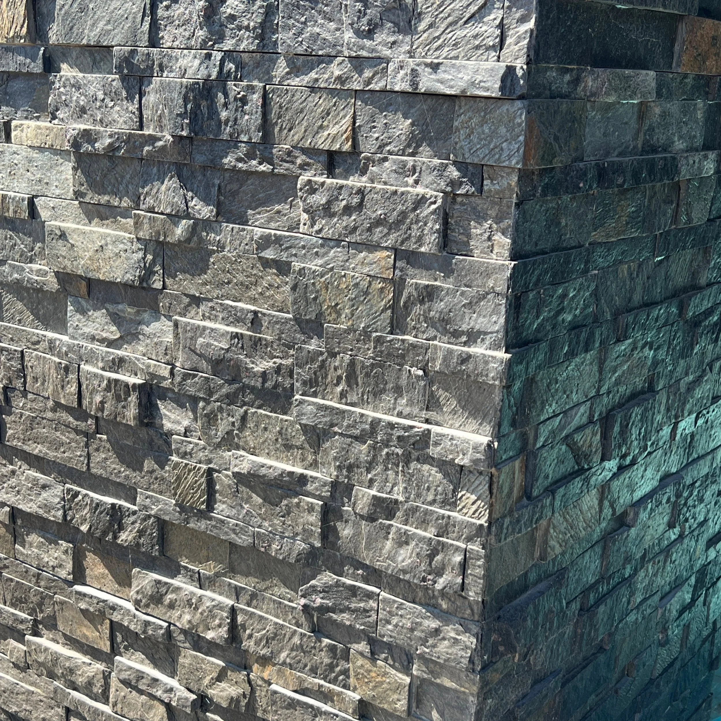 Close-up of a corner of a stone wall made of rectangular gray and greenish stones.