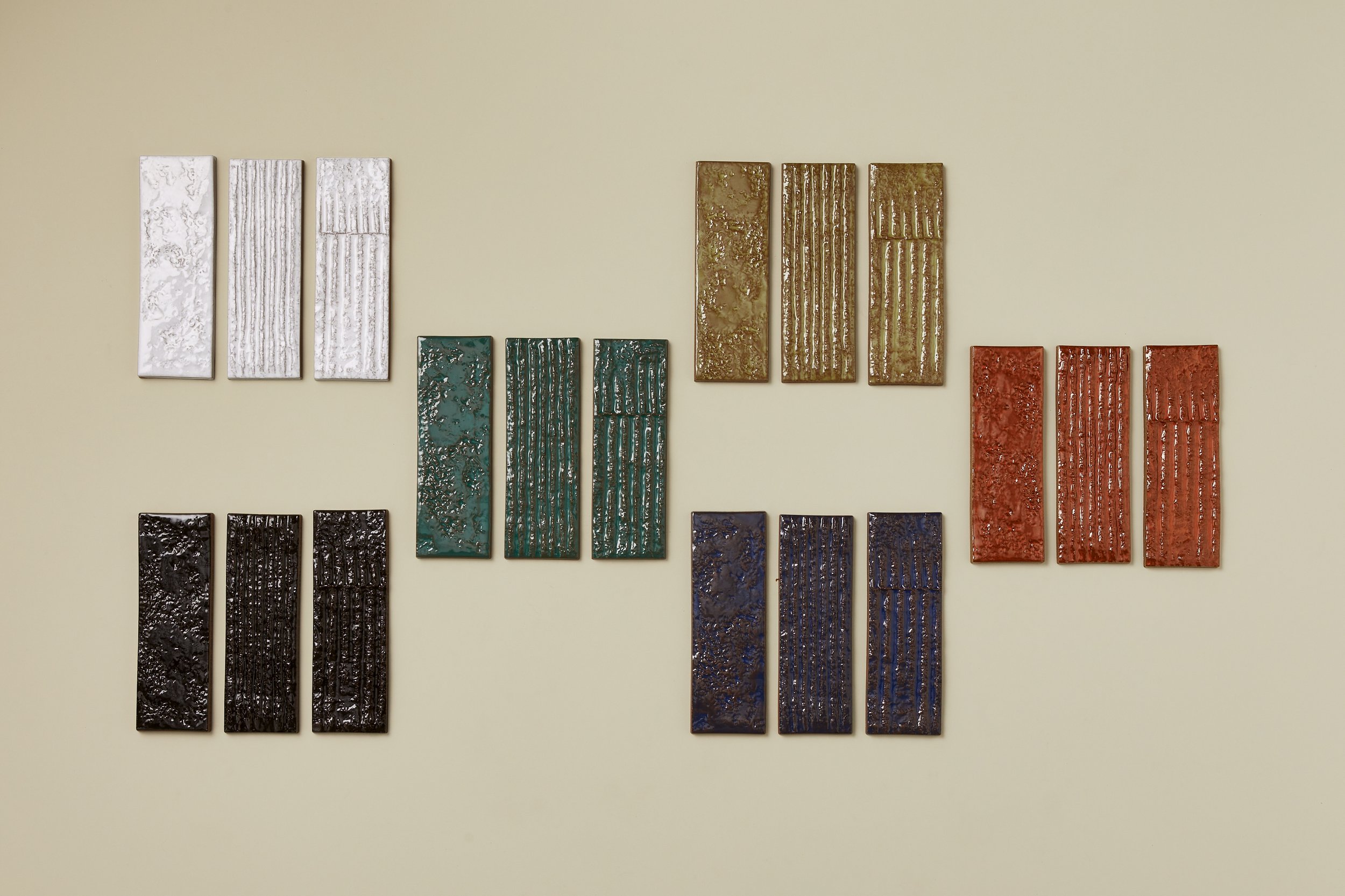 Set of nine textured ceramic wall art panels arranged in three groups of three, in white, green, brown, black, blue, and red, mounted on a beige wall.