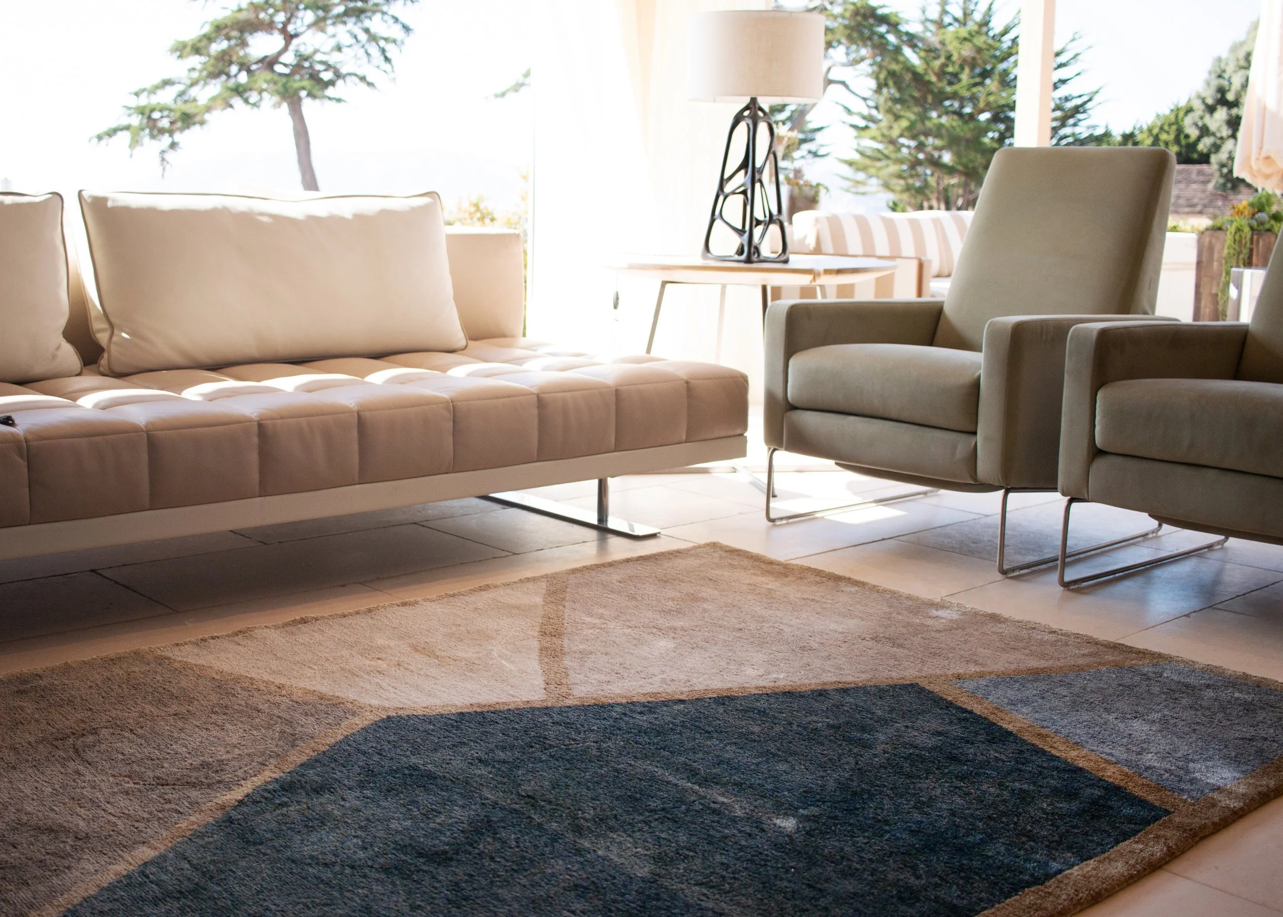 Living room with beige sofa, two matching armchairs, a table lamp, and a large window showing trees outside
