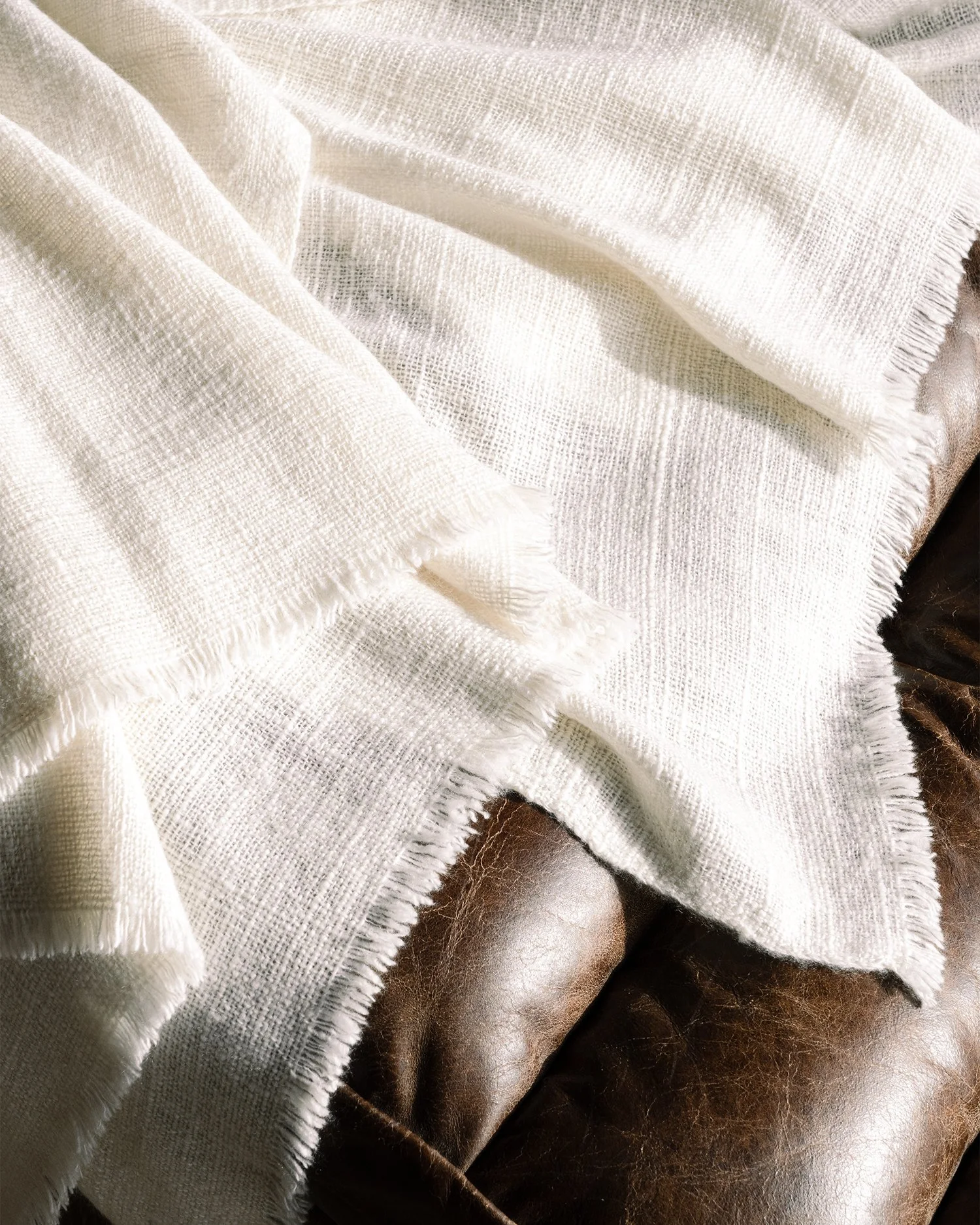Cream-colored woven fabric blanket draped over a dark brown leather surface.