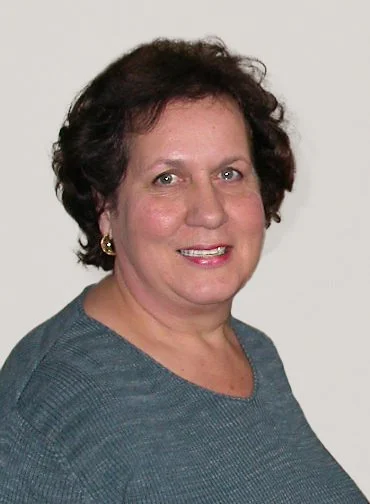 Black-and-white portrait of an older woman with curly hair, wearing a black top, facing slightly to the right, against a plain background.