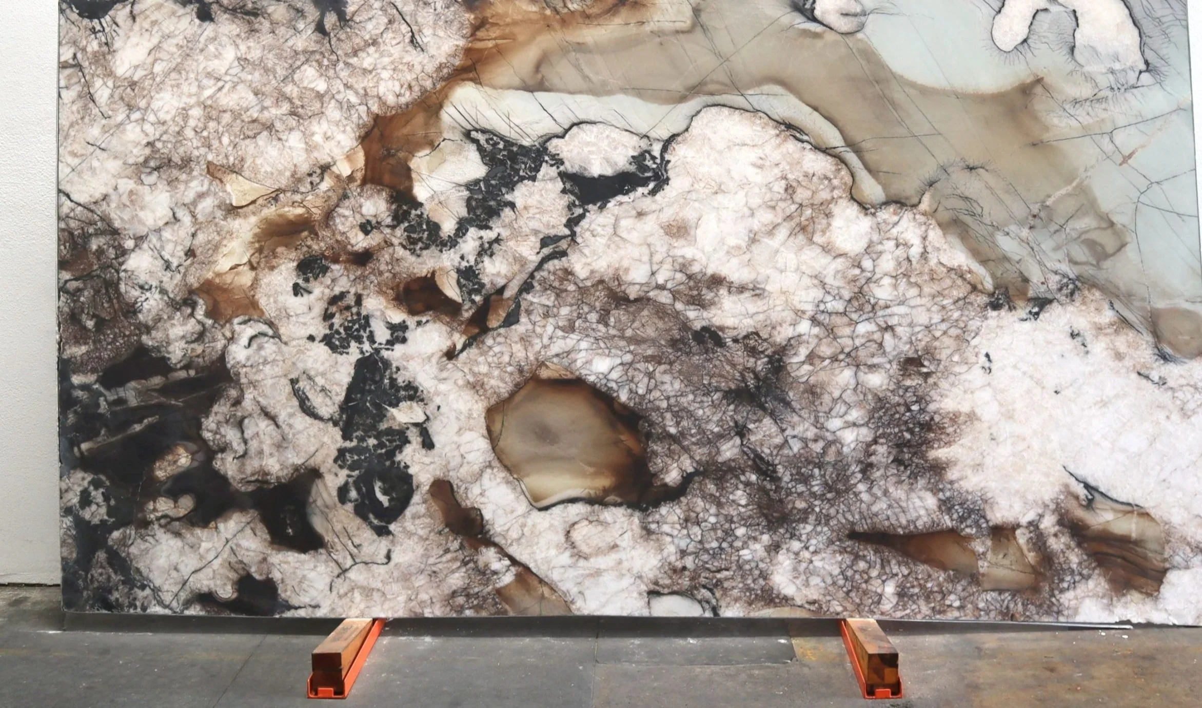 Large abstract marble stone slab with white, black, and brown mineral patterns, displayed on a stand in a warehouse or gallery.