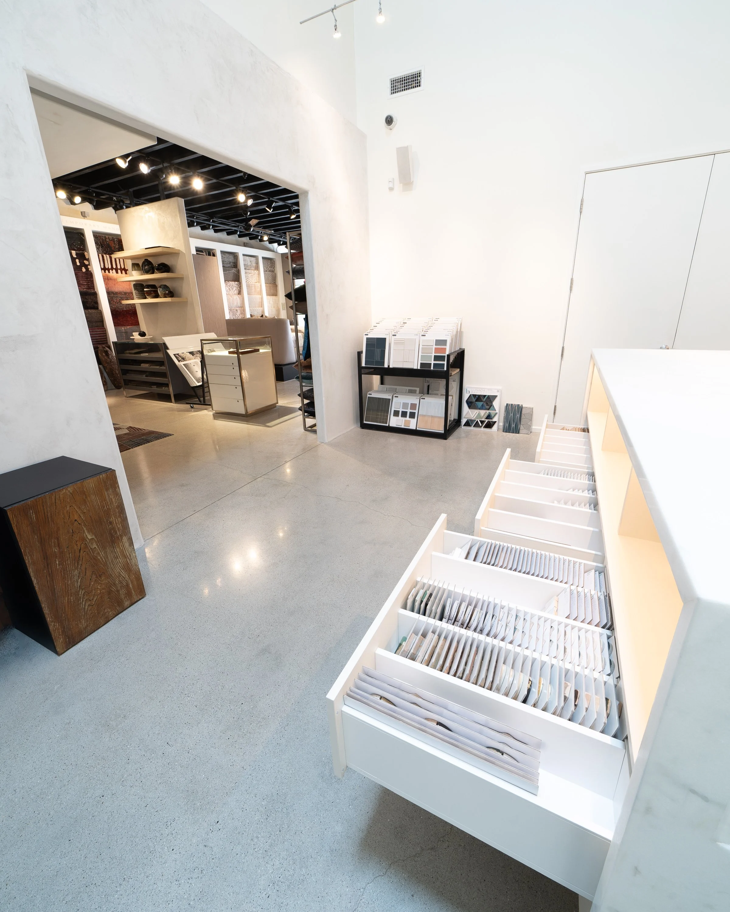 Interior of a showroom displaying fabric and material samples with white walls, polished concrete floors, and modern lighting.