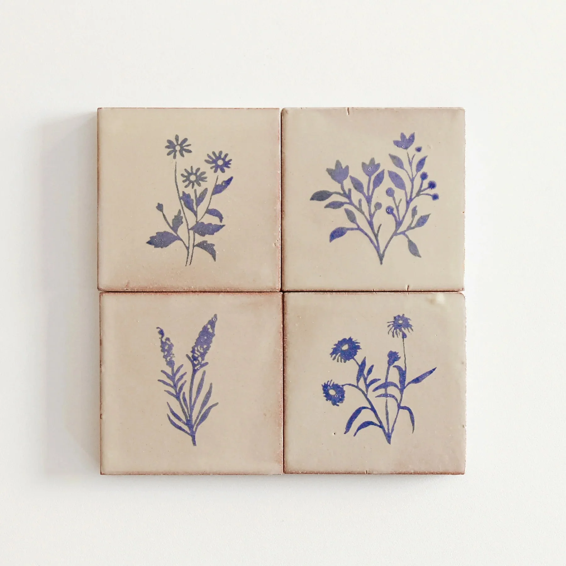 Four decorative ceramic tiles with purple floral illustrations arranged in a 2x2 grid, placed on a white surface