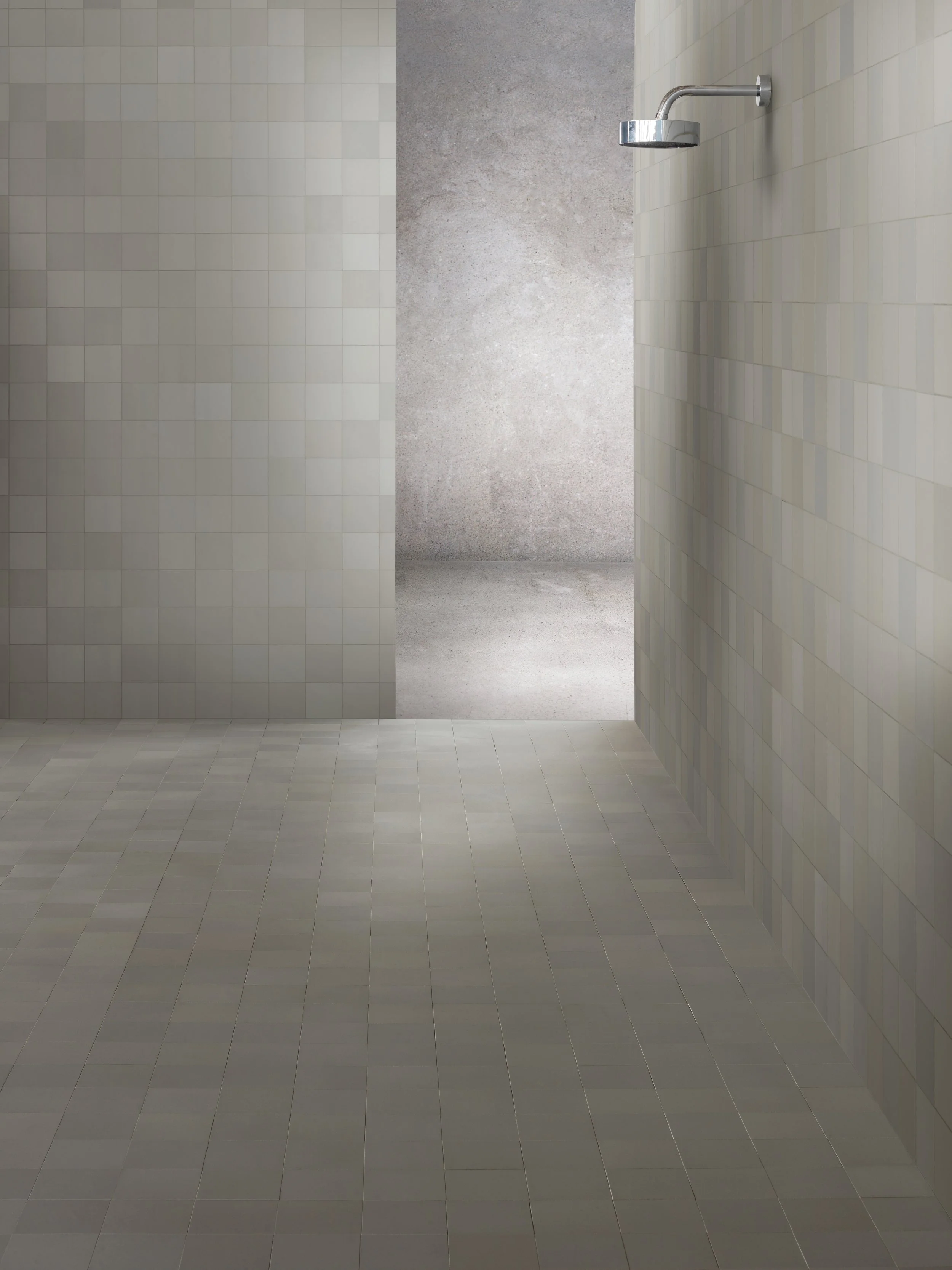 Empty shower area with a wall-mounted showerhead in a minimalistic bathroom with beige and gray tiled walls and floor.