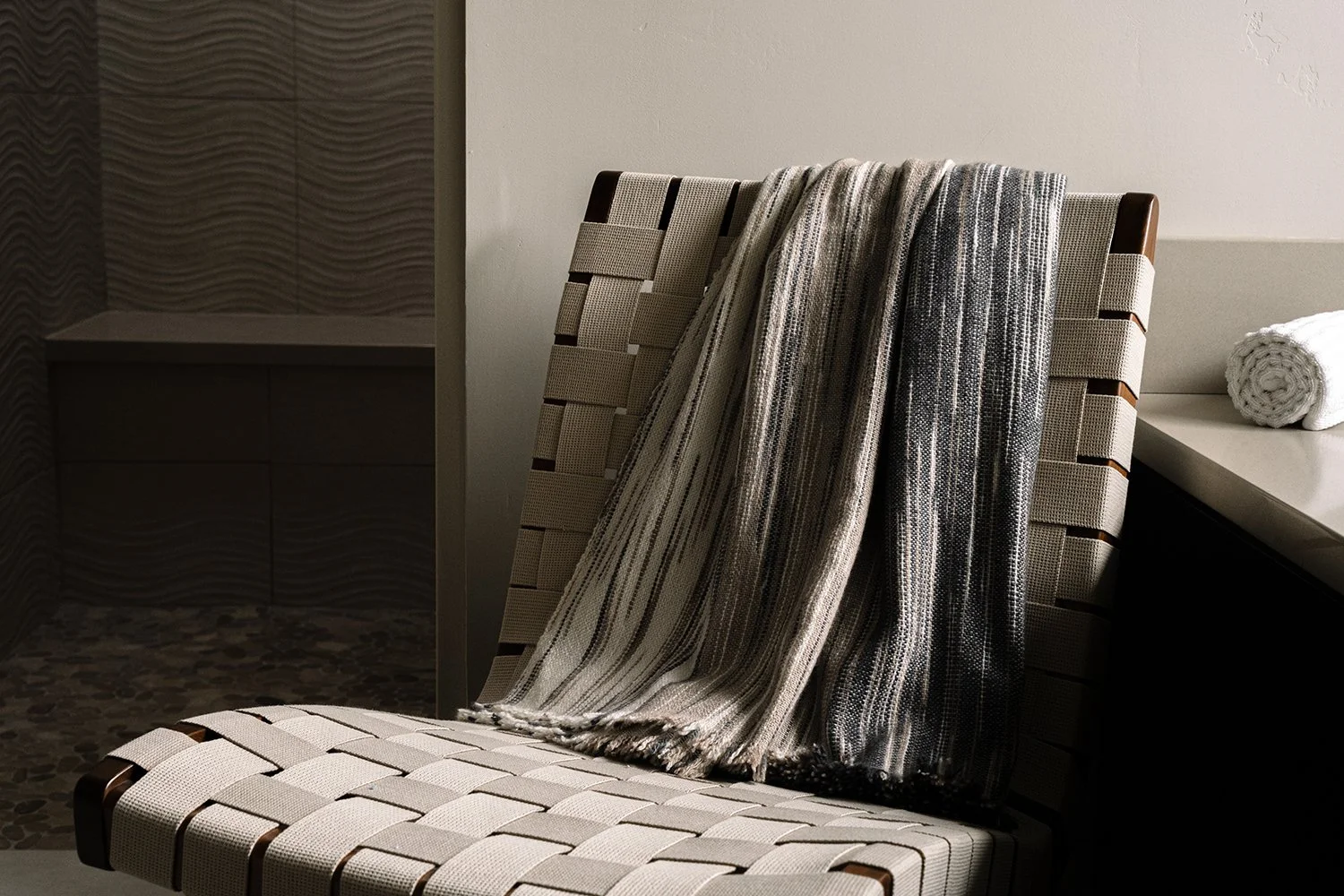 A tiled bench with a patterned fabric chair, over which a striped shawl and a towel are draped in a spa or bathroom setting.