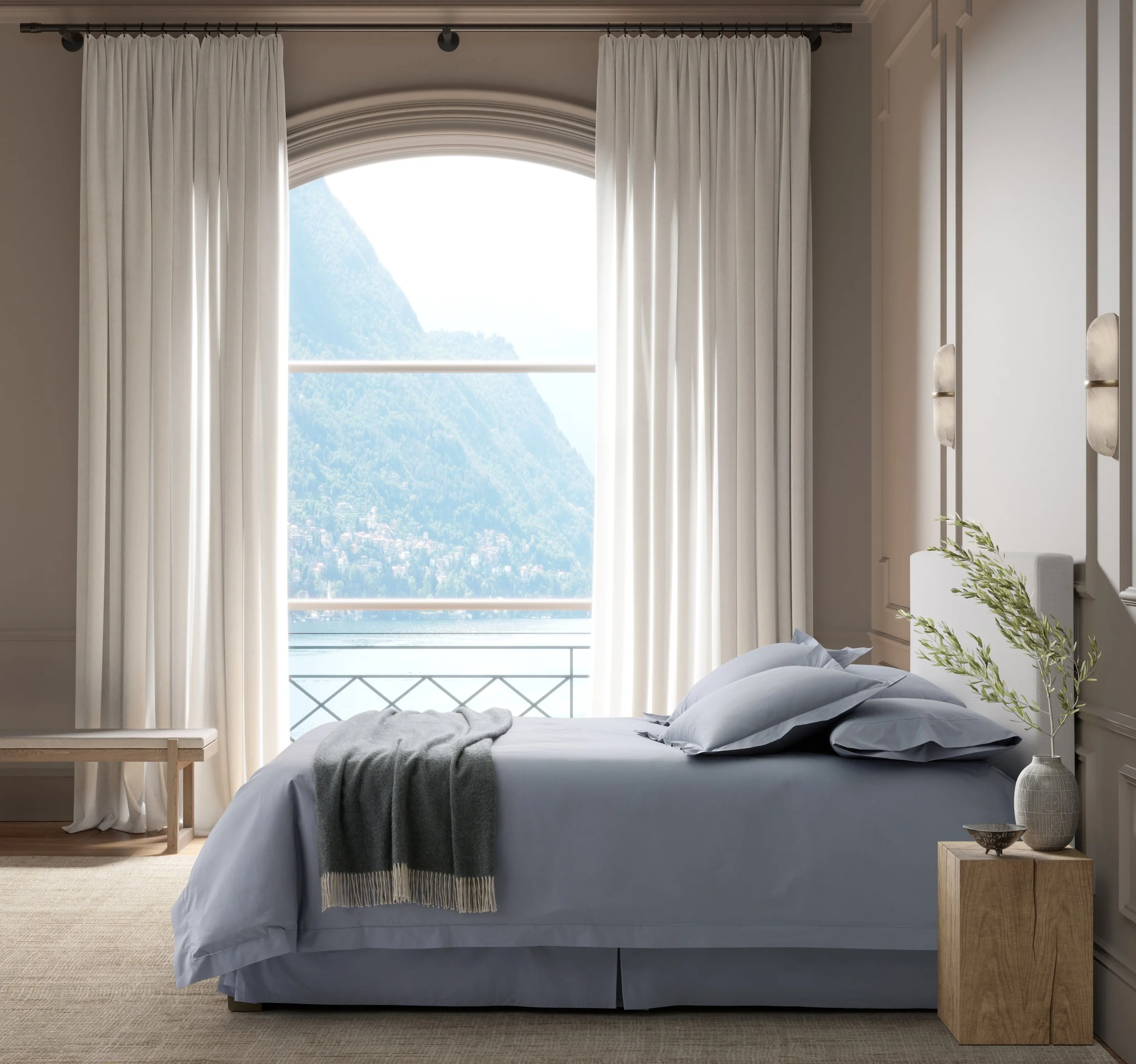 A cozy bedroom with a large window showing a mountain view, white curtains, a bed with blue pillows and blanket, a wooden side table with a vase and plant, and a bench at the foot of the bed.
