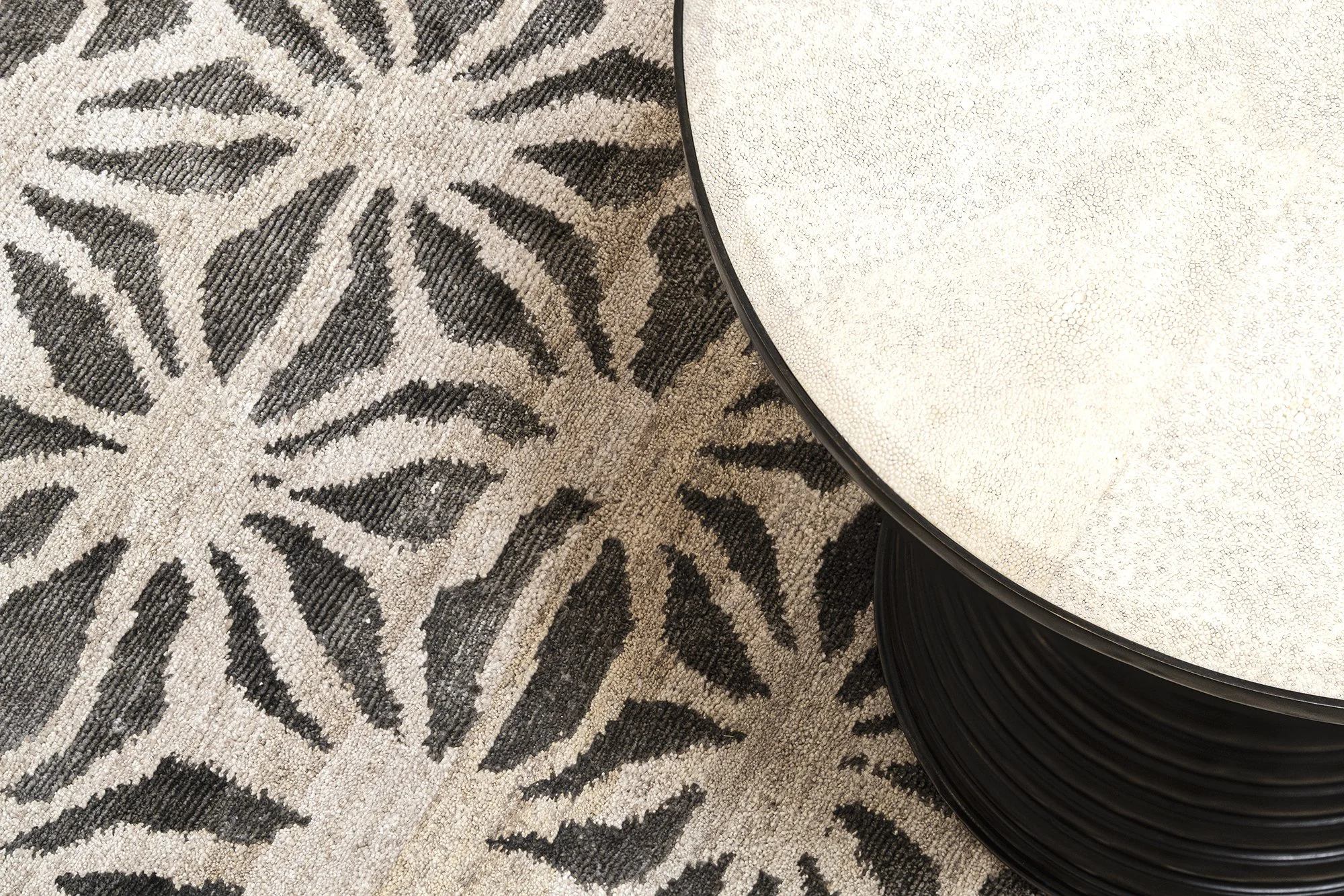 Close-up of a black and white patterned carpet next to a round, textured white table with a black rim.