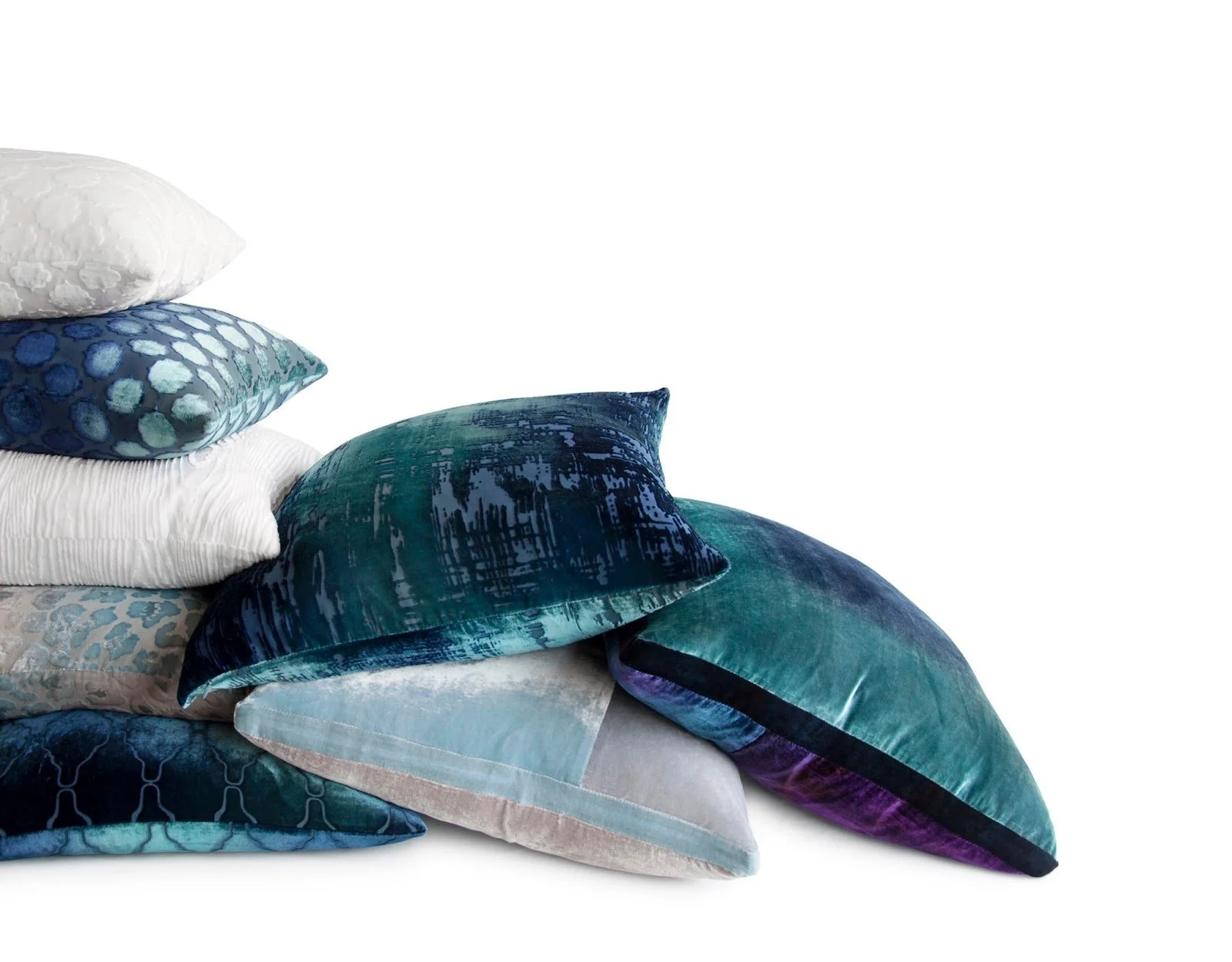 A stack of assorted decorative throw pillows in blue, teal, purple, and white colors with various patterns and textures, arranged on a plain white background.