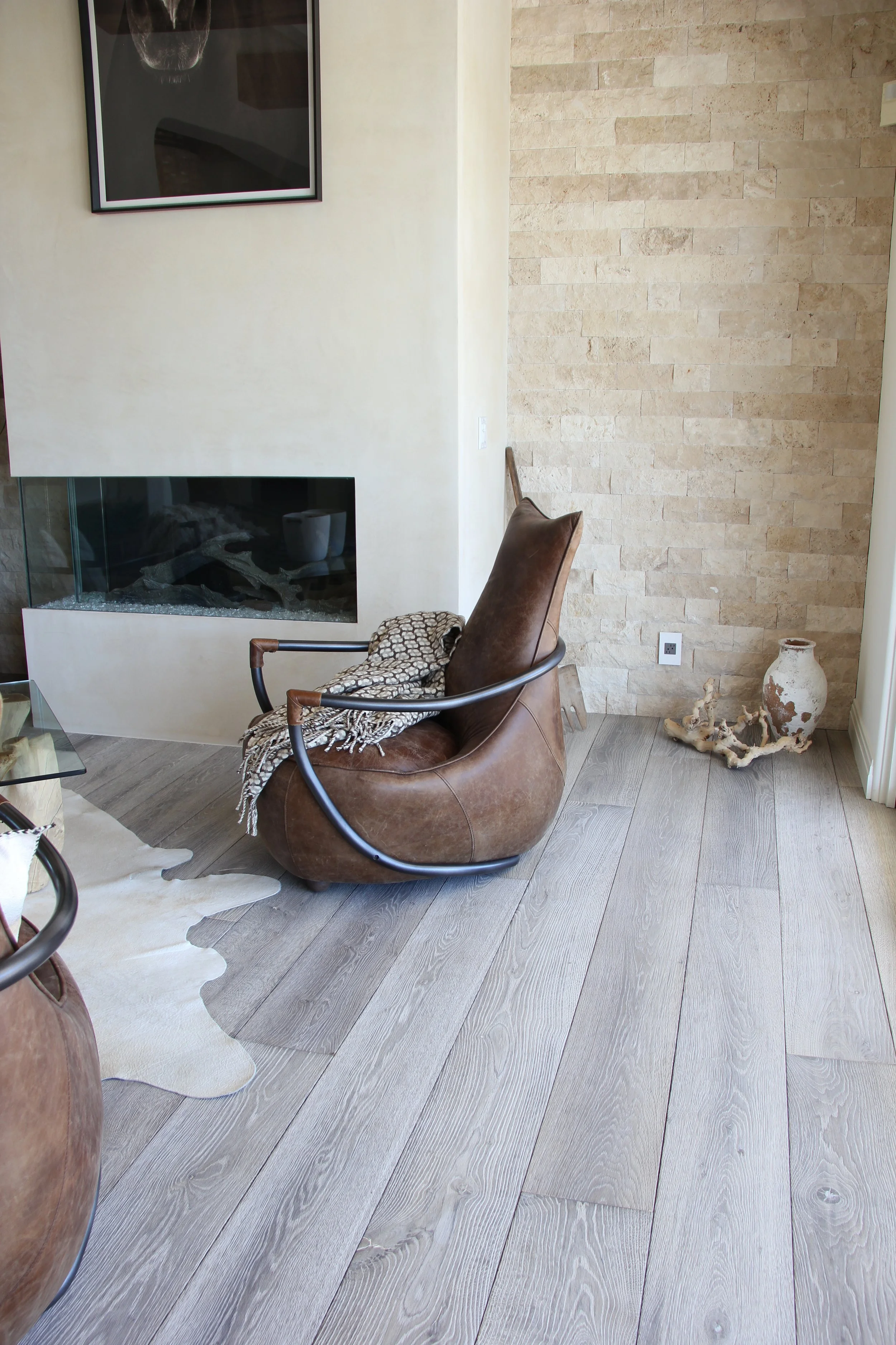 Modern living room corner with a leather armchair, a beige textured wall, a fireplace, and decorative items like a vase and driftwood.