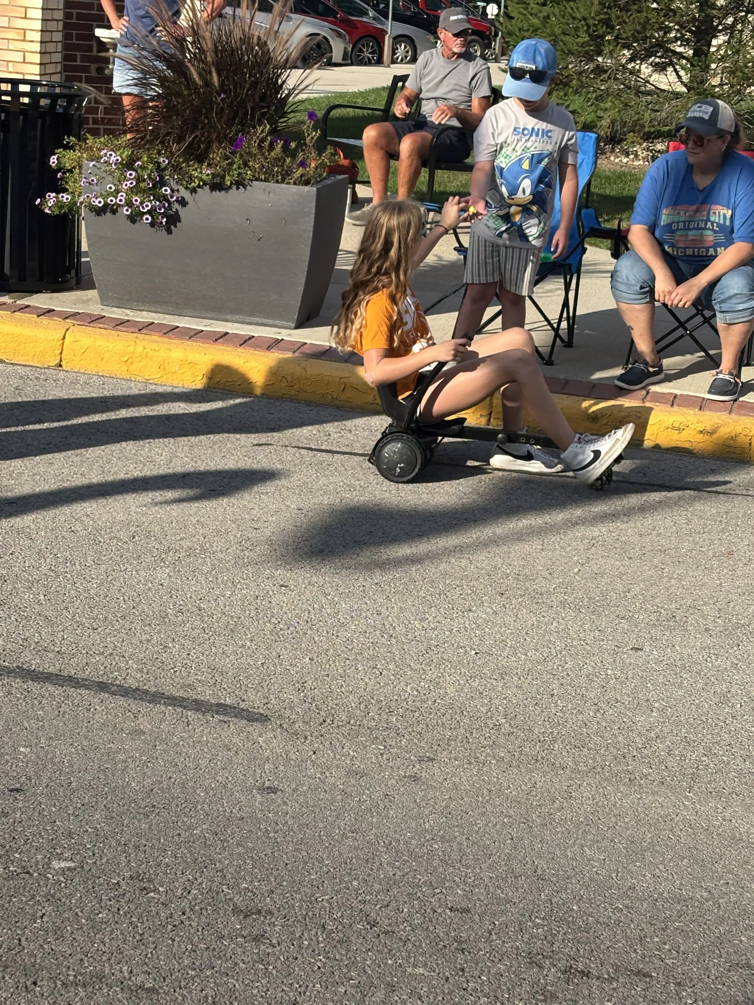 Young girl sitting on a wheeled mobility scooter on the street during Henry County Parade with spectators nearby