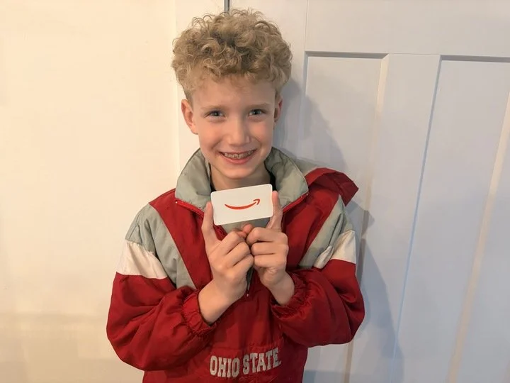 Child smiling and holding a gift card, representing participation in Shine Ortho Studio’s patient rewards or referral program.