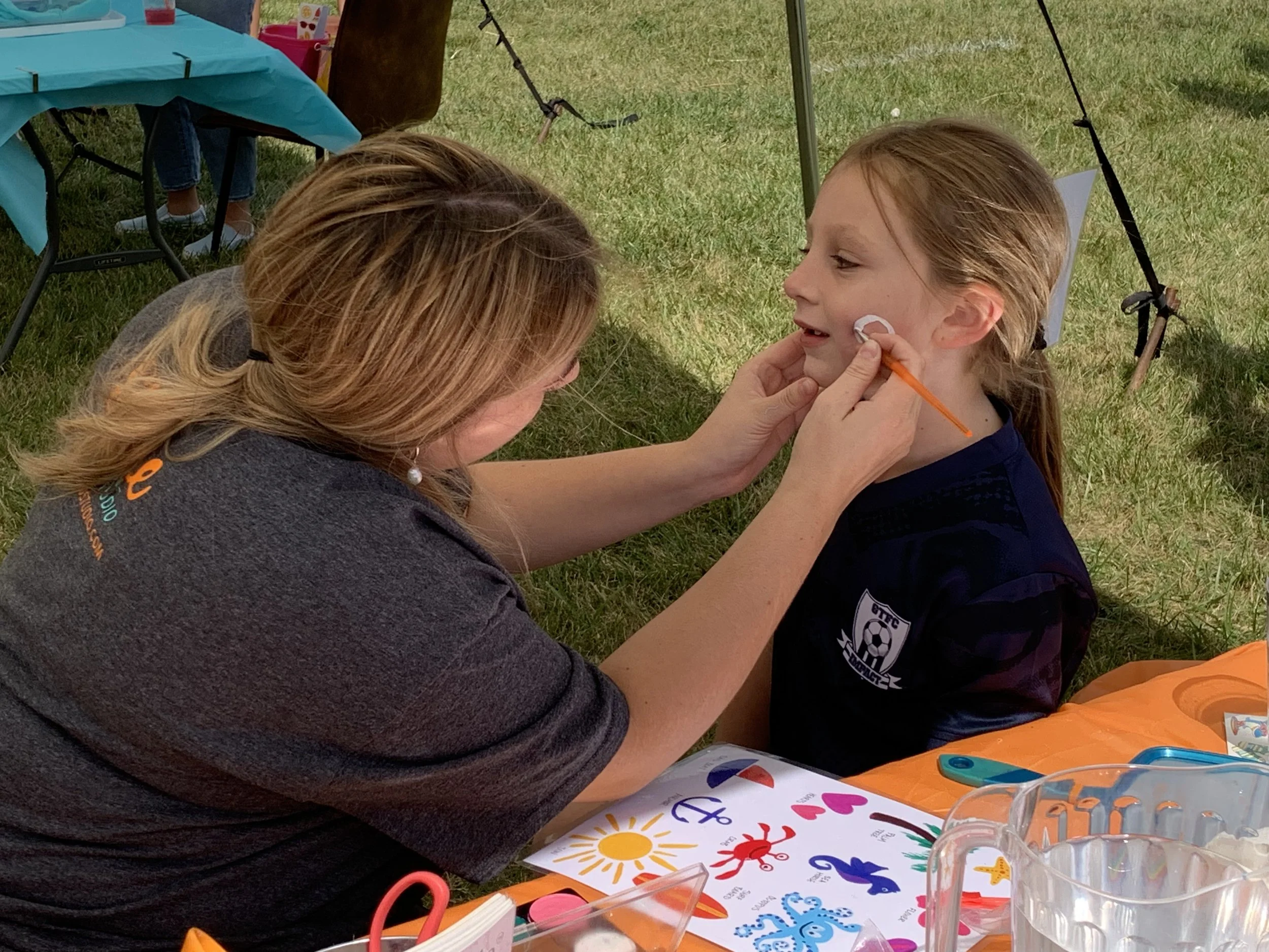 Shine Ortho Studio team member face painting a child during the new office open house community event.