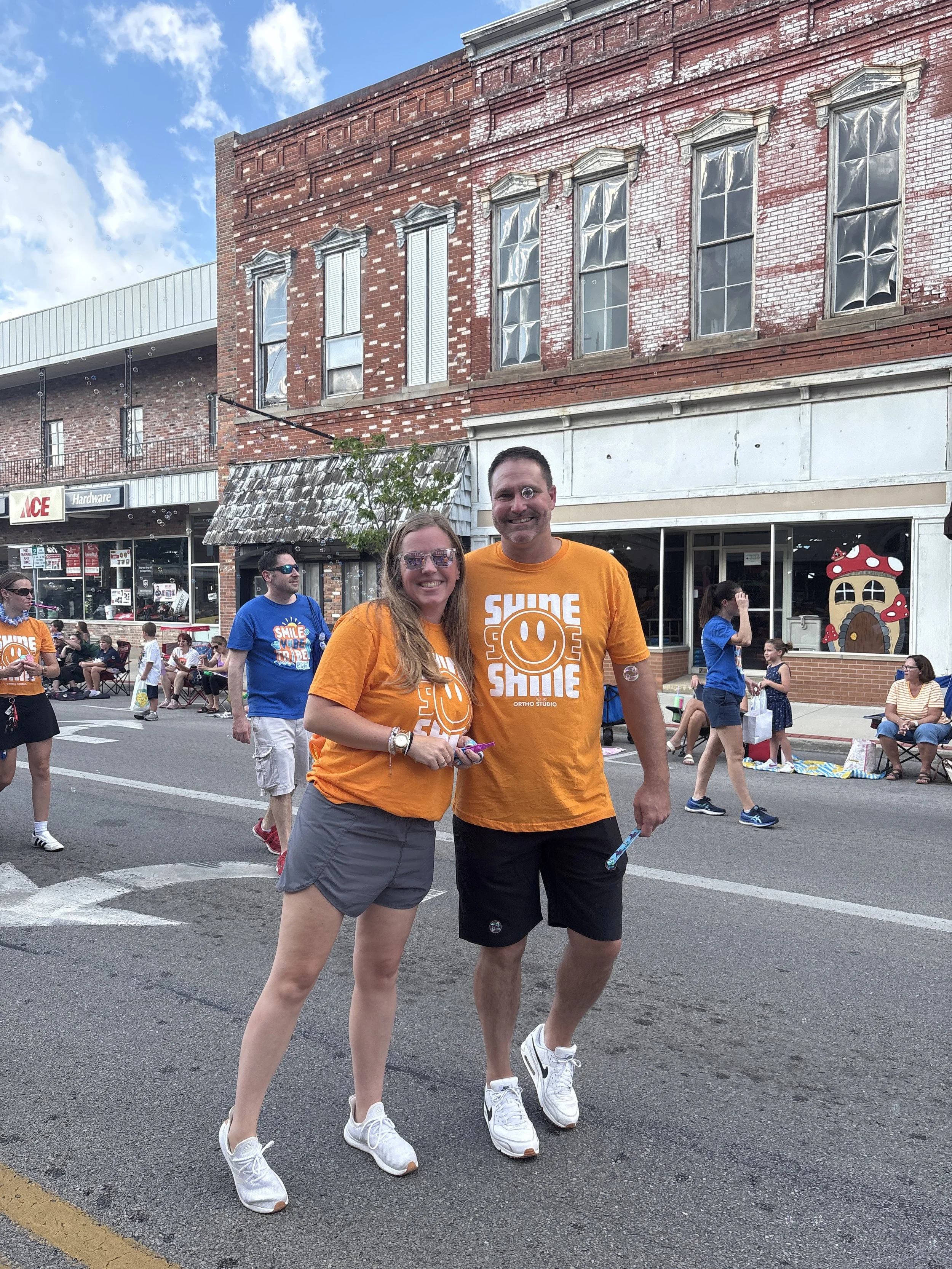 Shine Ortho Studio team members in orange shirts walking down the street at Henry County Parade handing out items to spectators