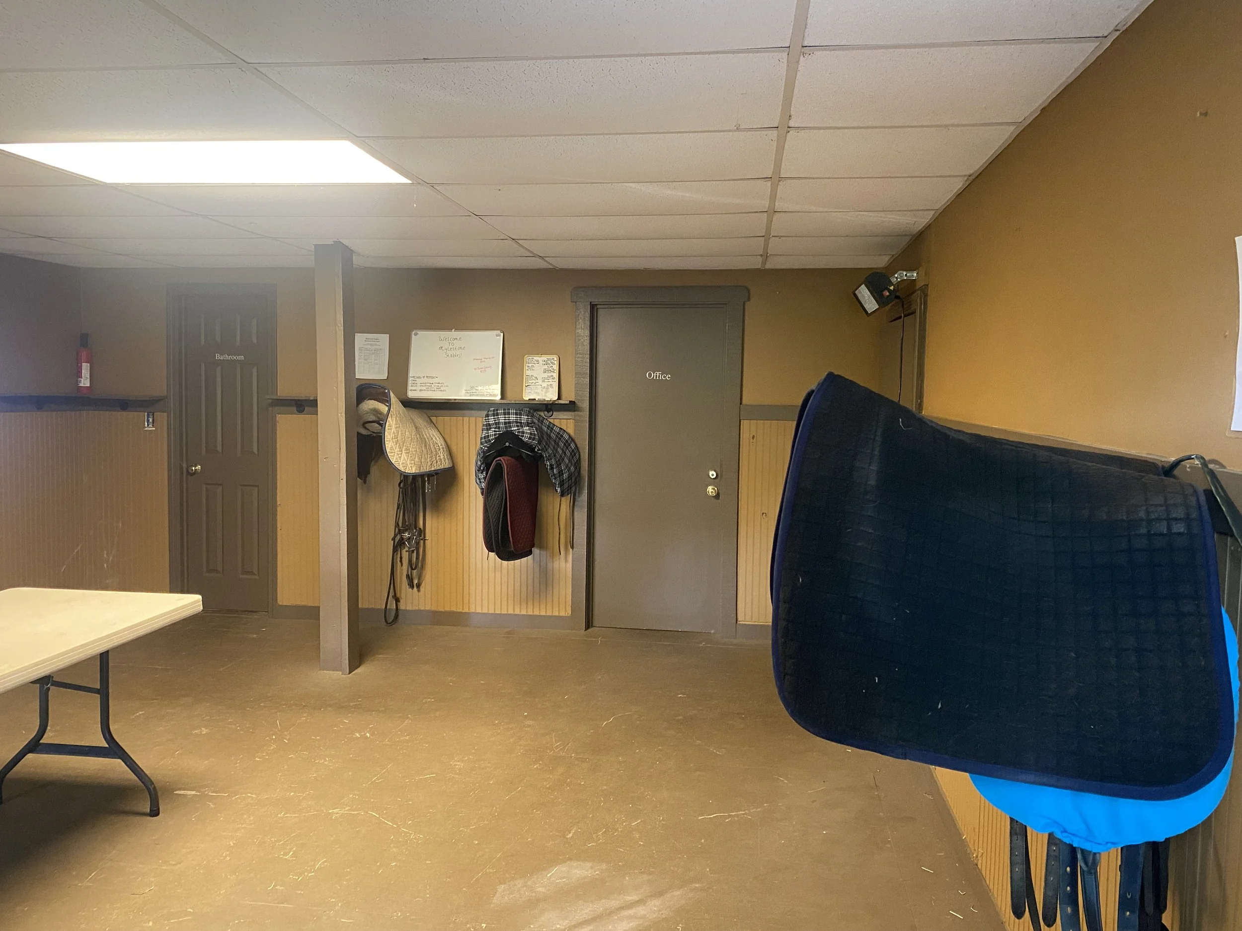 The main tack room with a table, tack, and horse riding gear.