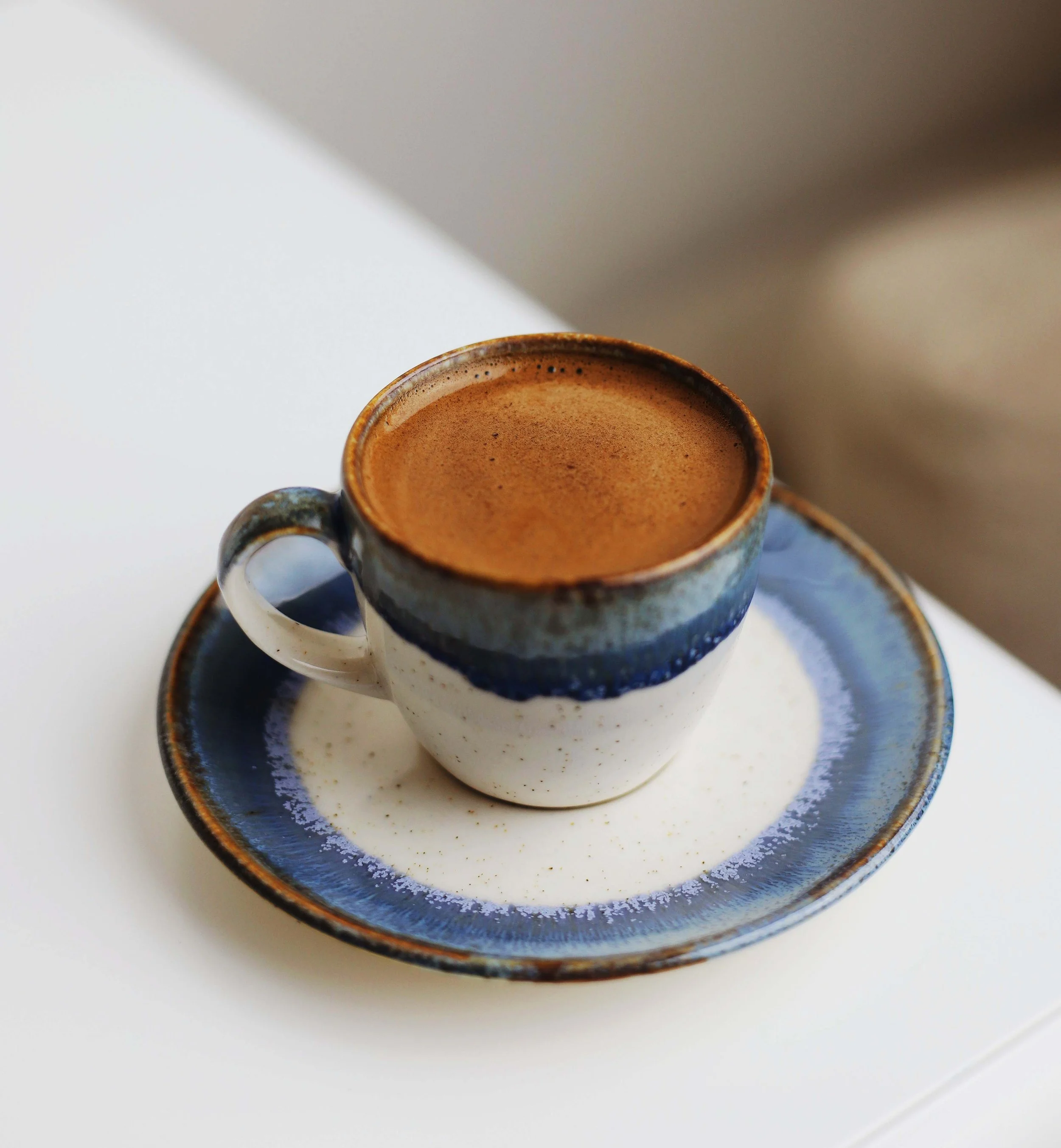 A cup of coffee in a blue and white ceramic mug on a white table.