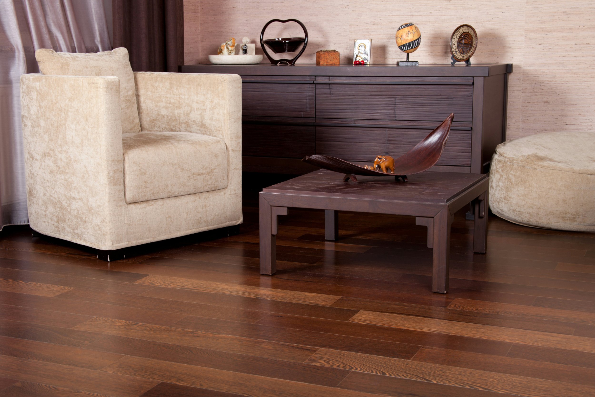 Living room with beige armchair, dark wood dresser with decorative objects, and a dark wood coffee table with a wooden boat sculpture