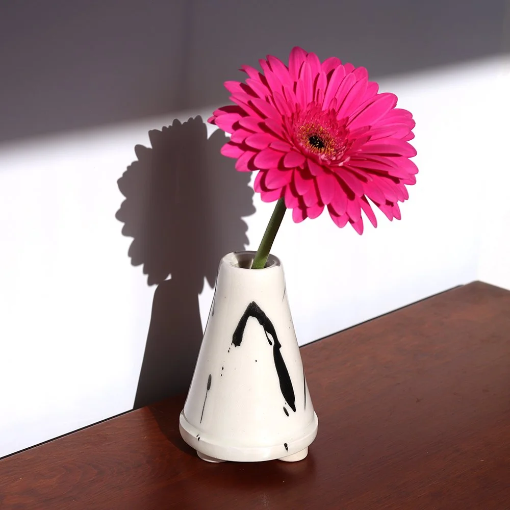 A pink gerbera daisy in a white ceramic vase on a wooden surface, casting a shadow on the wall behind.