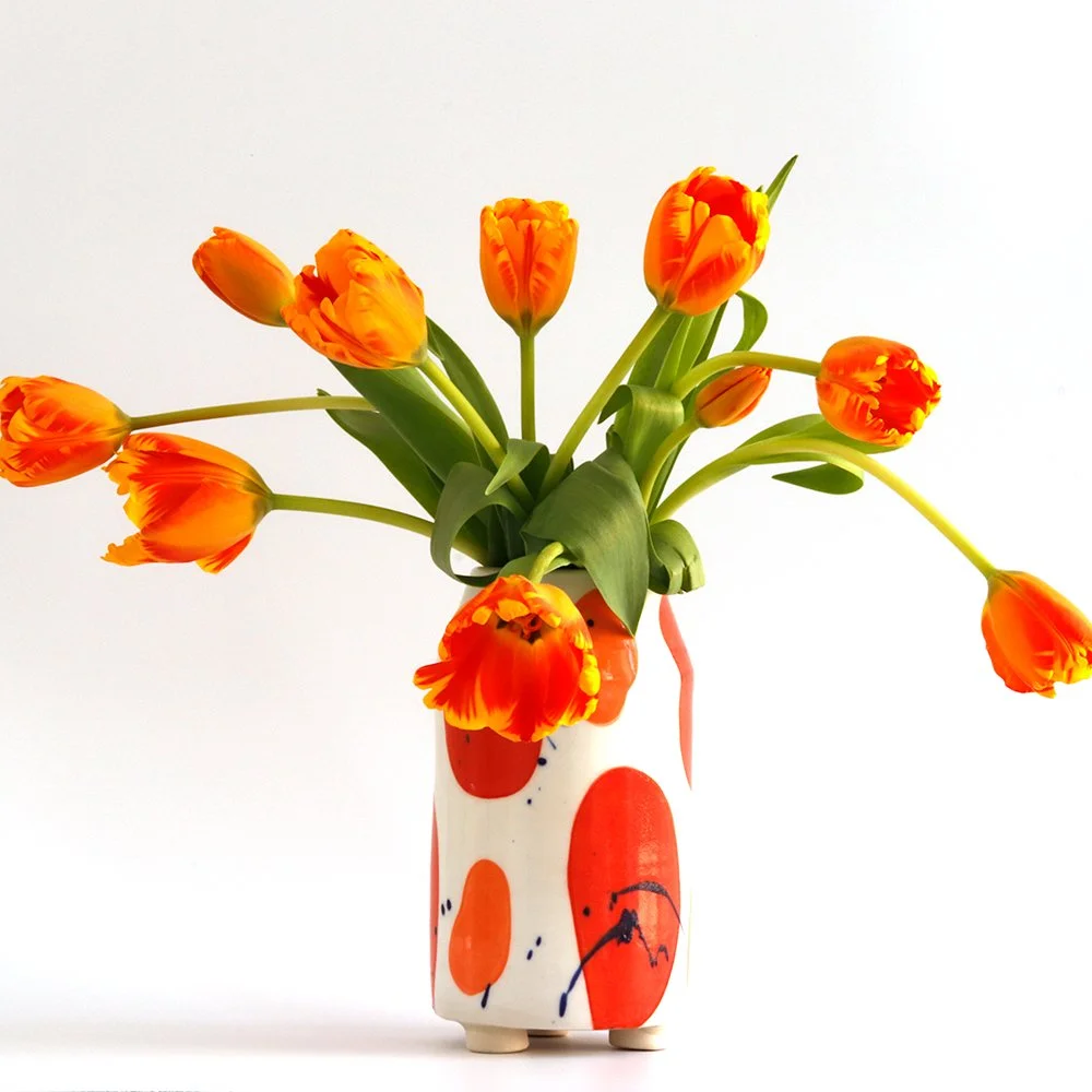 Orange tulips in a colorful, abstract-patterned white vase with orange and red shapes.