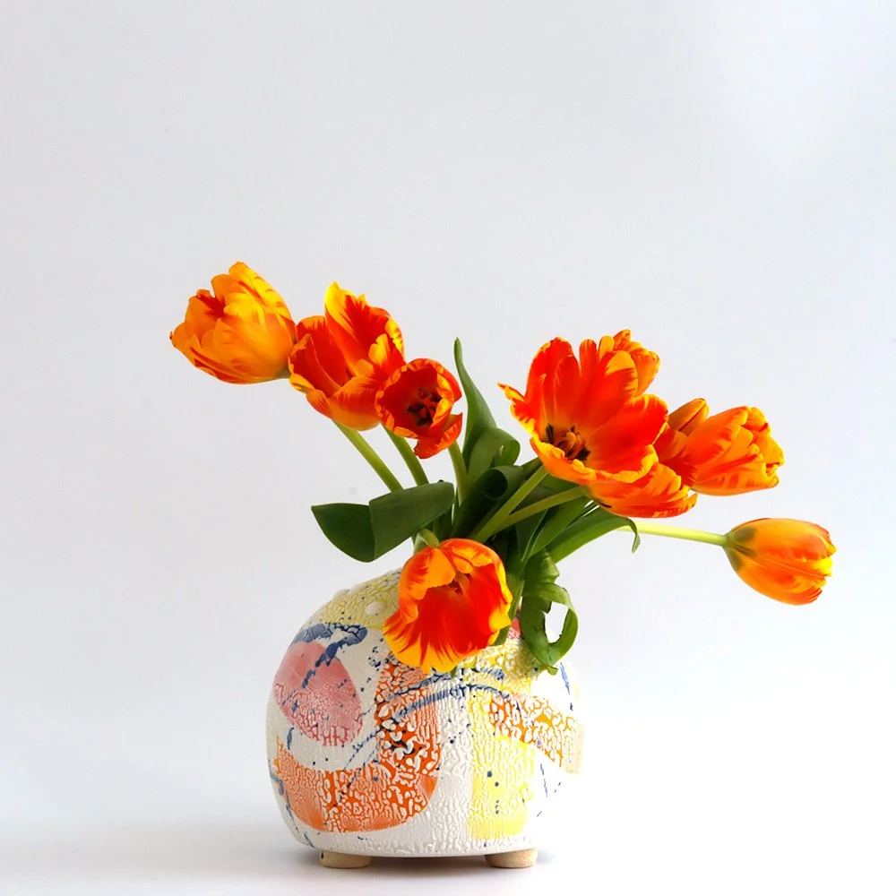 Orange tulips in a colorful decorative vase against a white background.