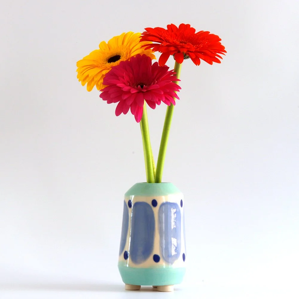 Three colorful flowers in a patterned ceramic vase on a white background.