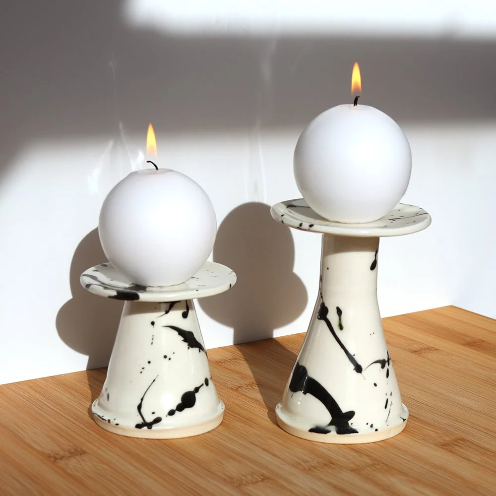 Two white spherical candles with flames, placed on black and white marbled ceramic candle holders on a wooden surface.