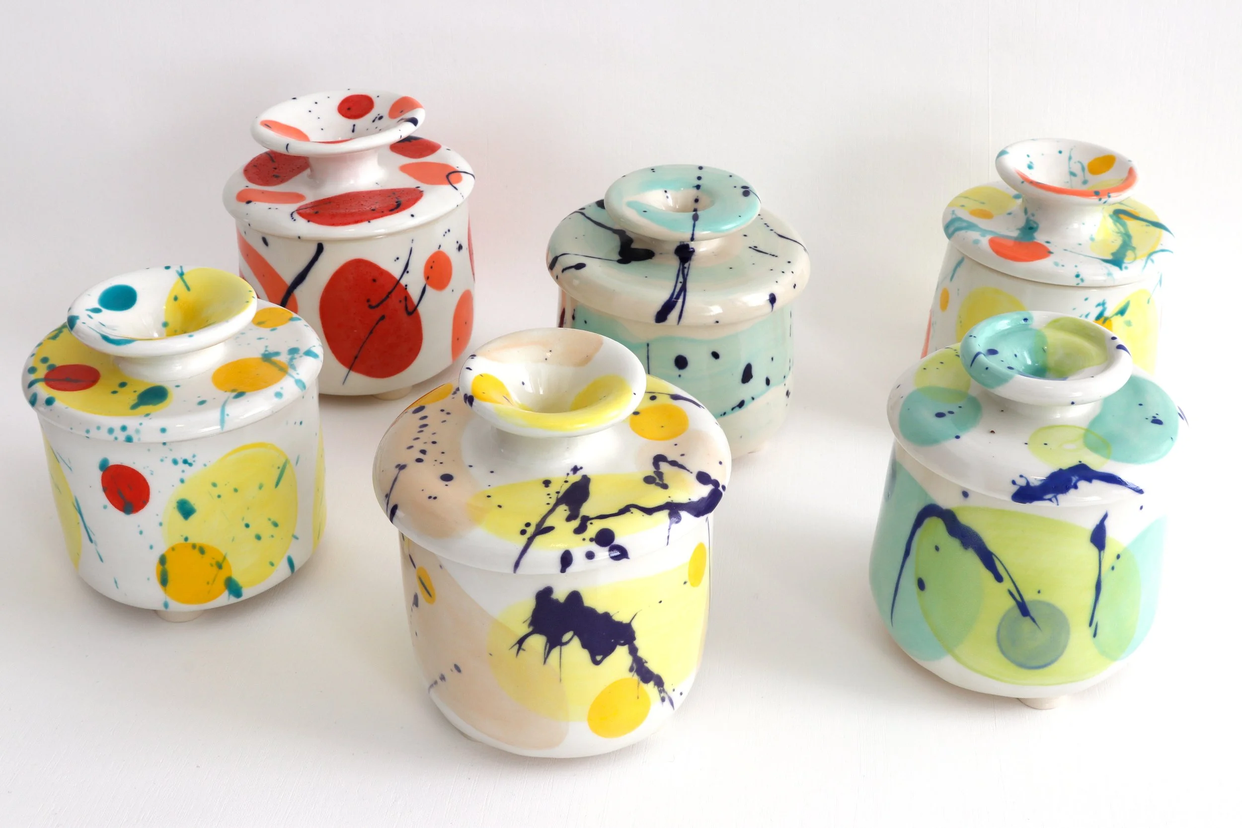 Six colorful decorated jars with lids on a white surface.