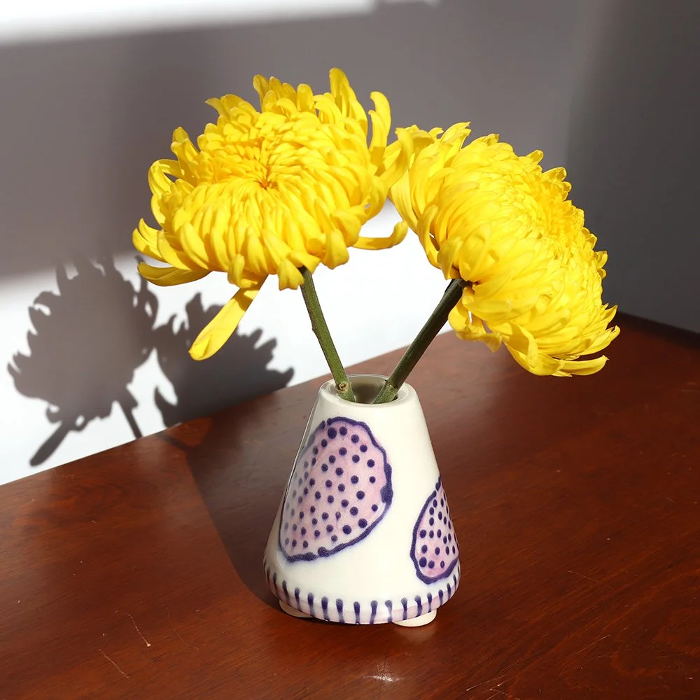Yellow chrysanthemums in a decorative white vase with purple designs, placed on a wooden surface.