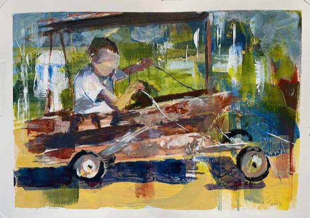 A child with a mask on sitting in a small vehicle or go-kart, holding a steering wheel, with a blurred background suggesting an outdoor setting.